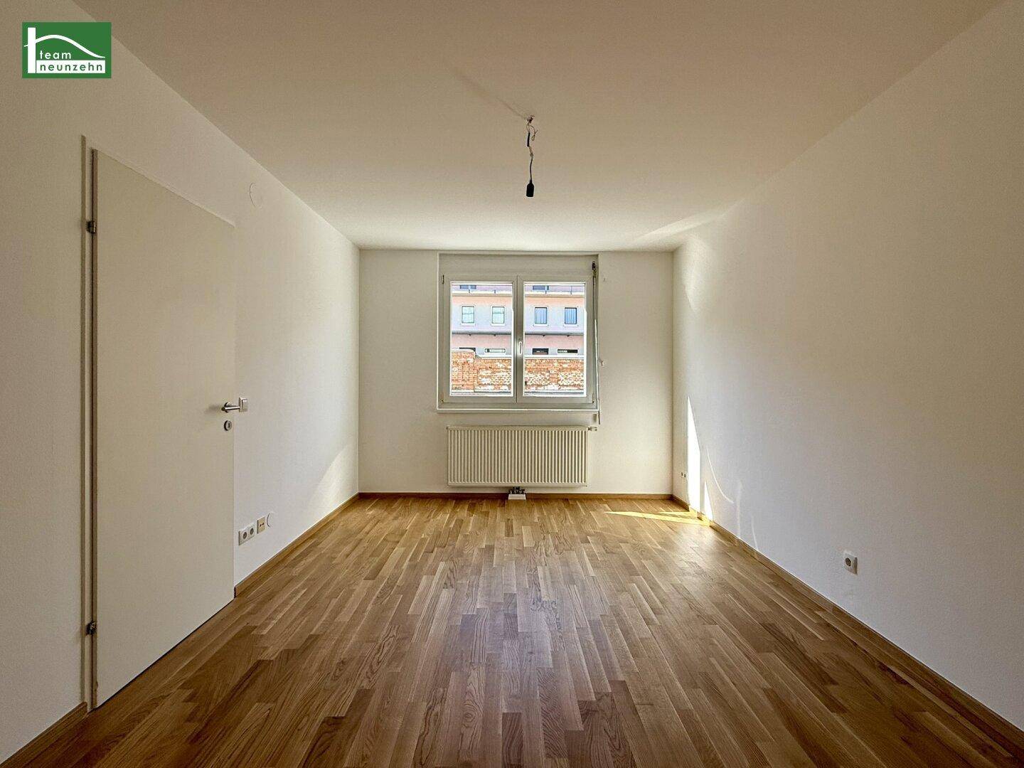 Leeres Schlafzimmer mit Holzparkettboden, weiß gestrichenen Wänden und einem Fenster.