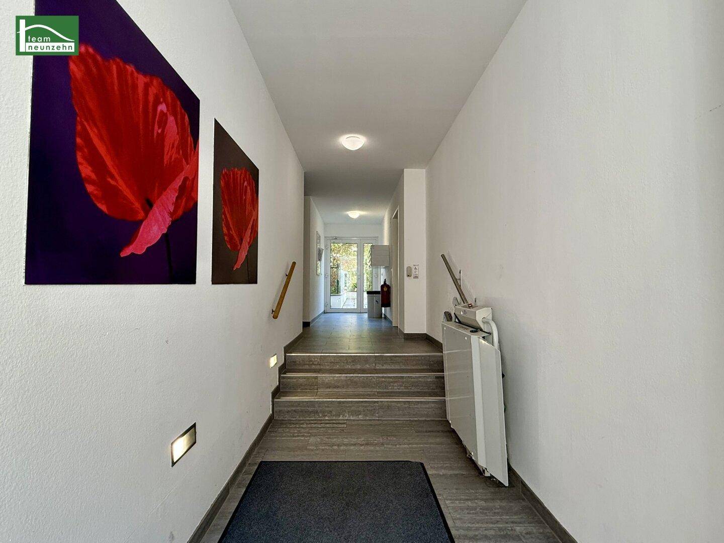 Treppenhaus mit Treppenlift, Kunstwerken an der Wand und Zugang zu weiteren Bereichen, barrierefrei gestaltet.