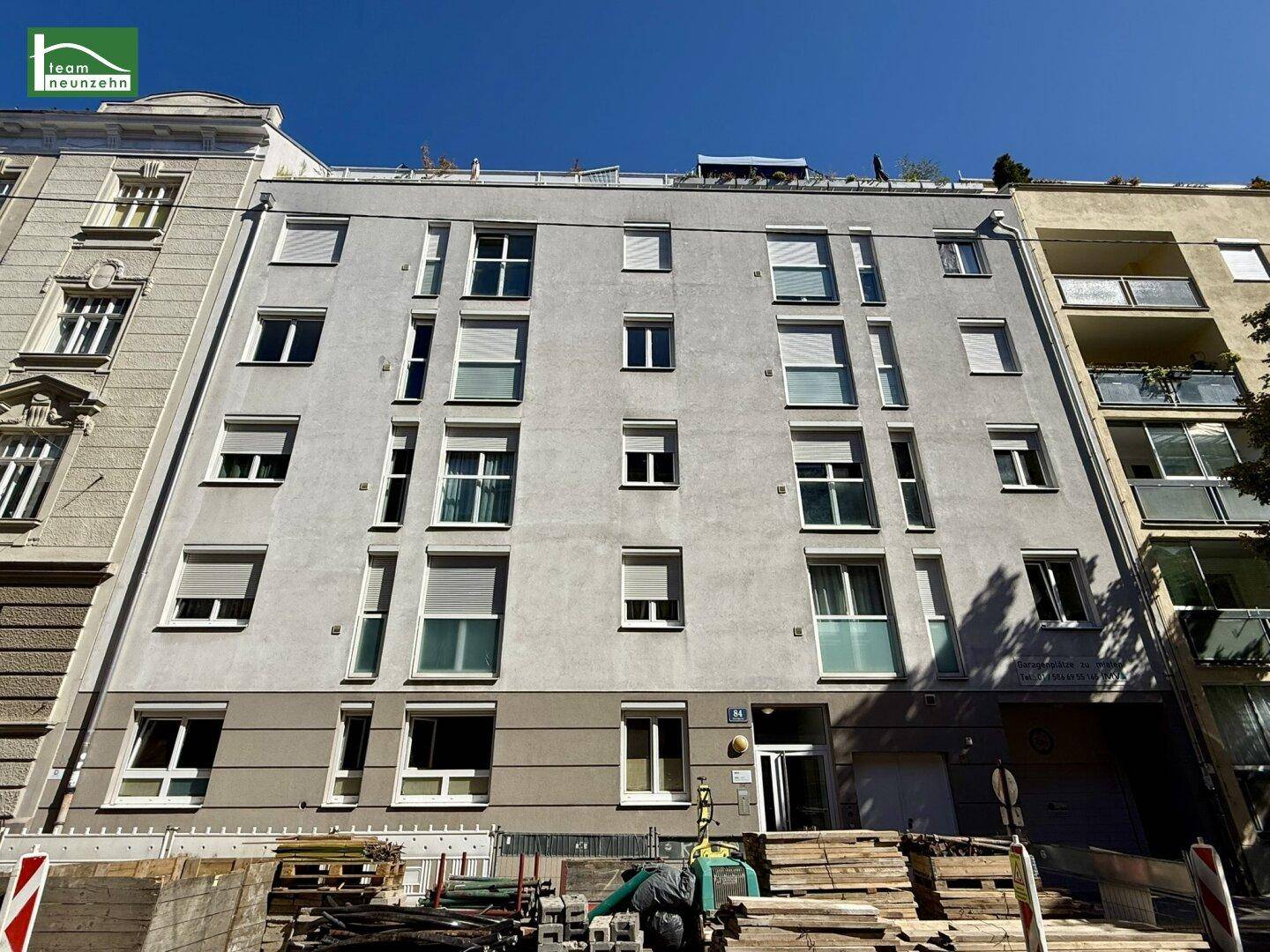 Modernes Wohngebäude mit mehreren Etagen, vielen Fenstern und Baustelle im Vordergrund.