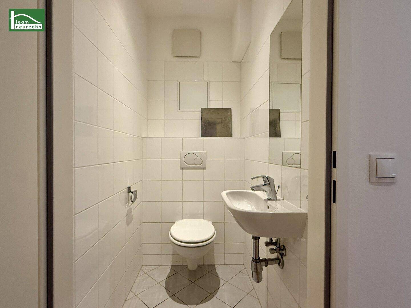 Kleines Gäste-WC mit weißen Fliesen, wandhängender Toilette und Waschbecken.
