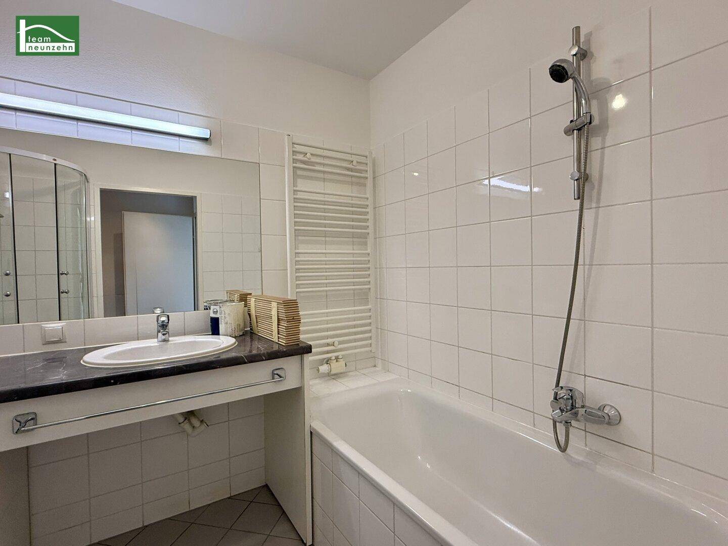 Badezimmer mit Badewanne, Waschtisch und beheiztem Handtuchhalter an der Wand.