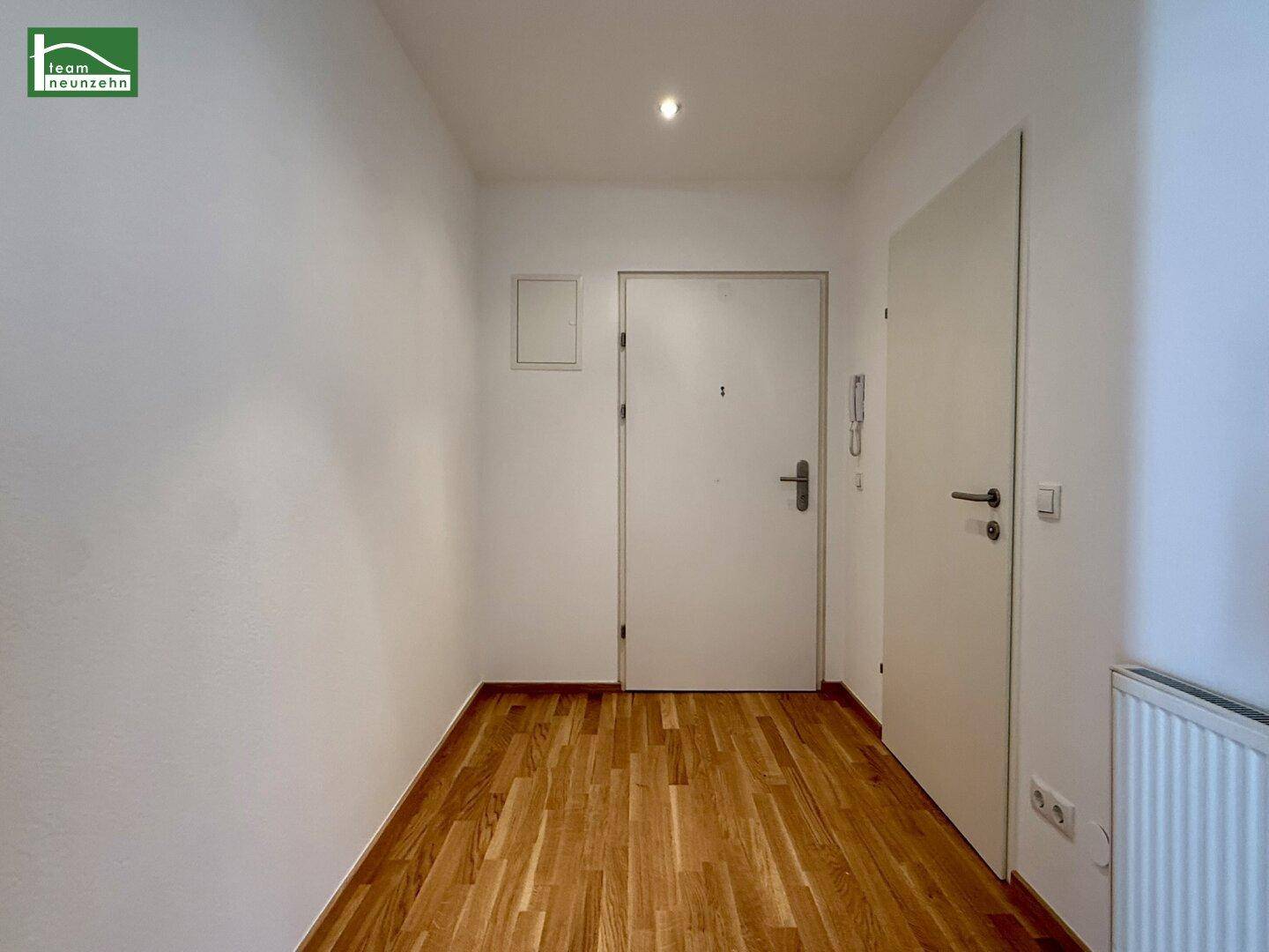 Heller Flur mit Holzparkettboden, weiß gestrichenen Wänden und Eingangstür.
