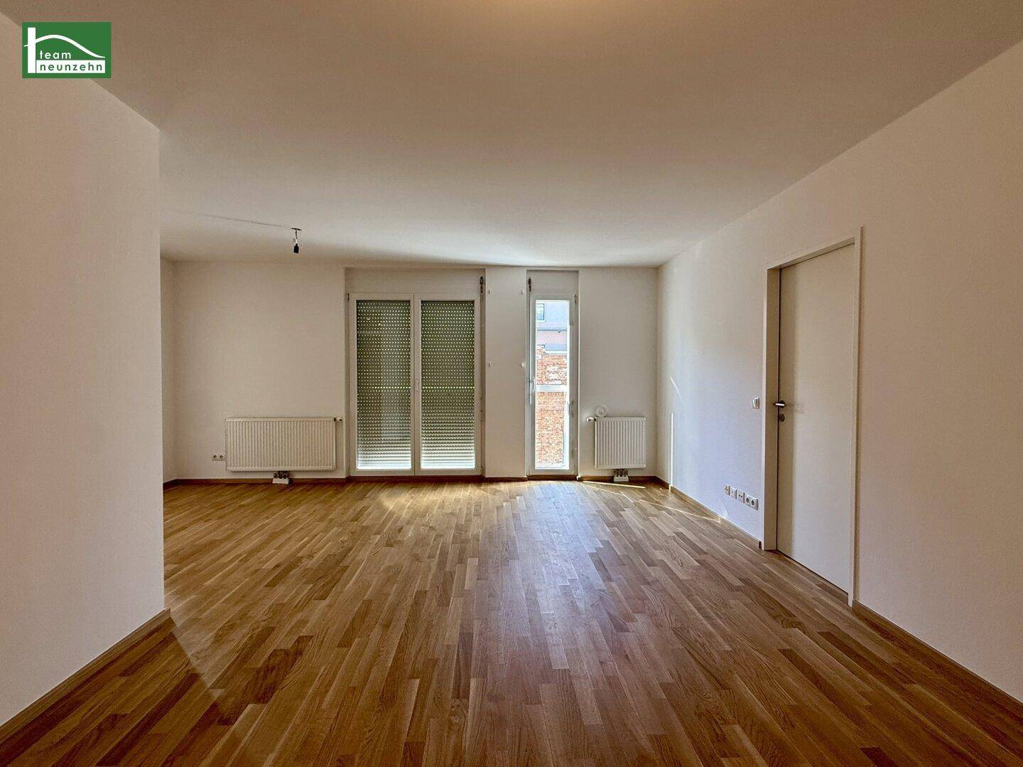 Heller Wohnbereich mit Holzparkettboden und Zugang zu einem Balkon oder einer Loggia.