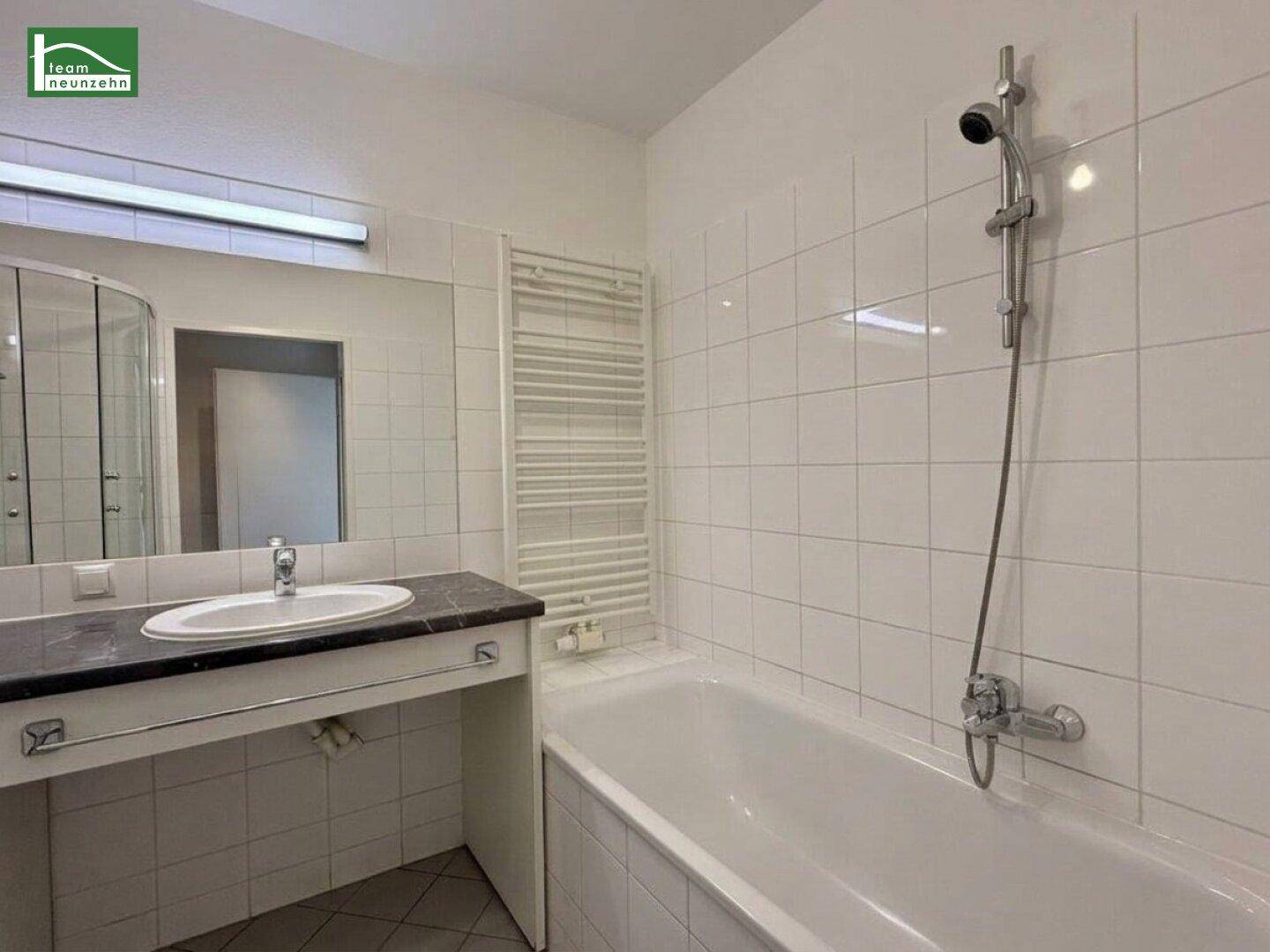 Badezimmer mit Badewanne, Waschbecken mit Ablage und einem beheizten Handtuchhalter, hell und praktisch eingerichtet.