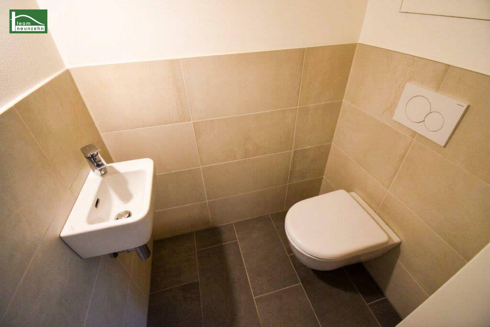 Modernes Gäste-WC mit Wand-WC, kleinem Waschbecken und beigefarbenen Fliesen.
