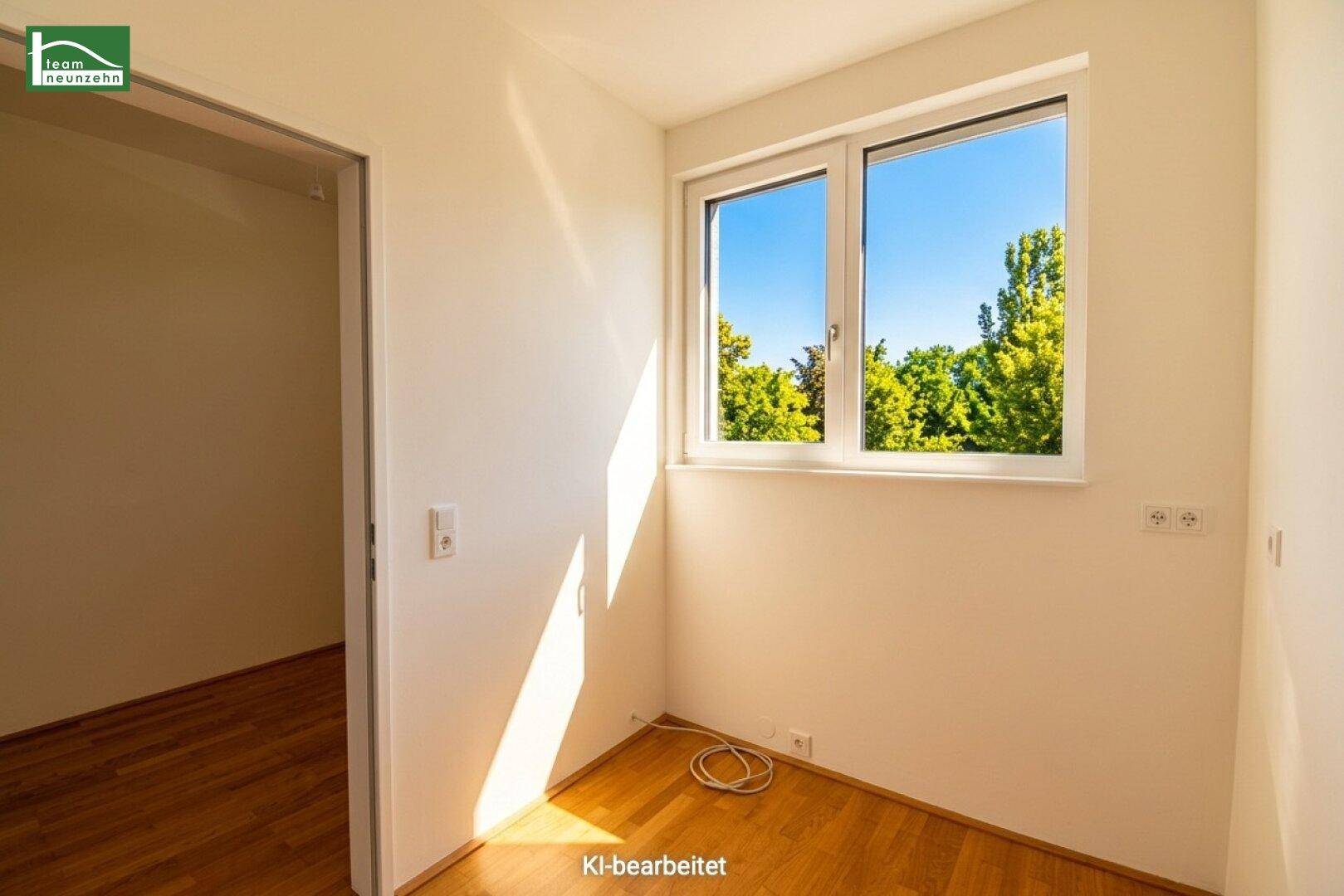 Helles Zimmer mit Holzboden und großem Fenster mit Blick ins Grüne.