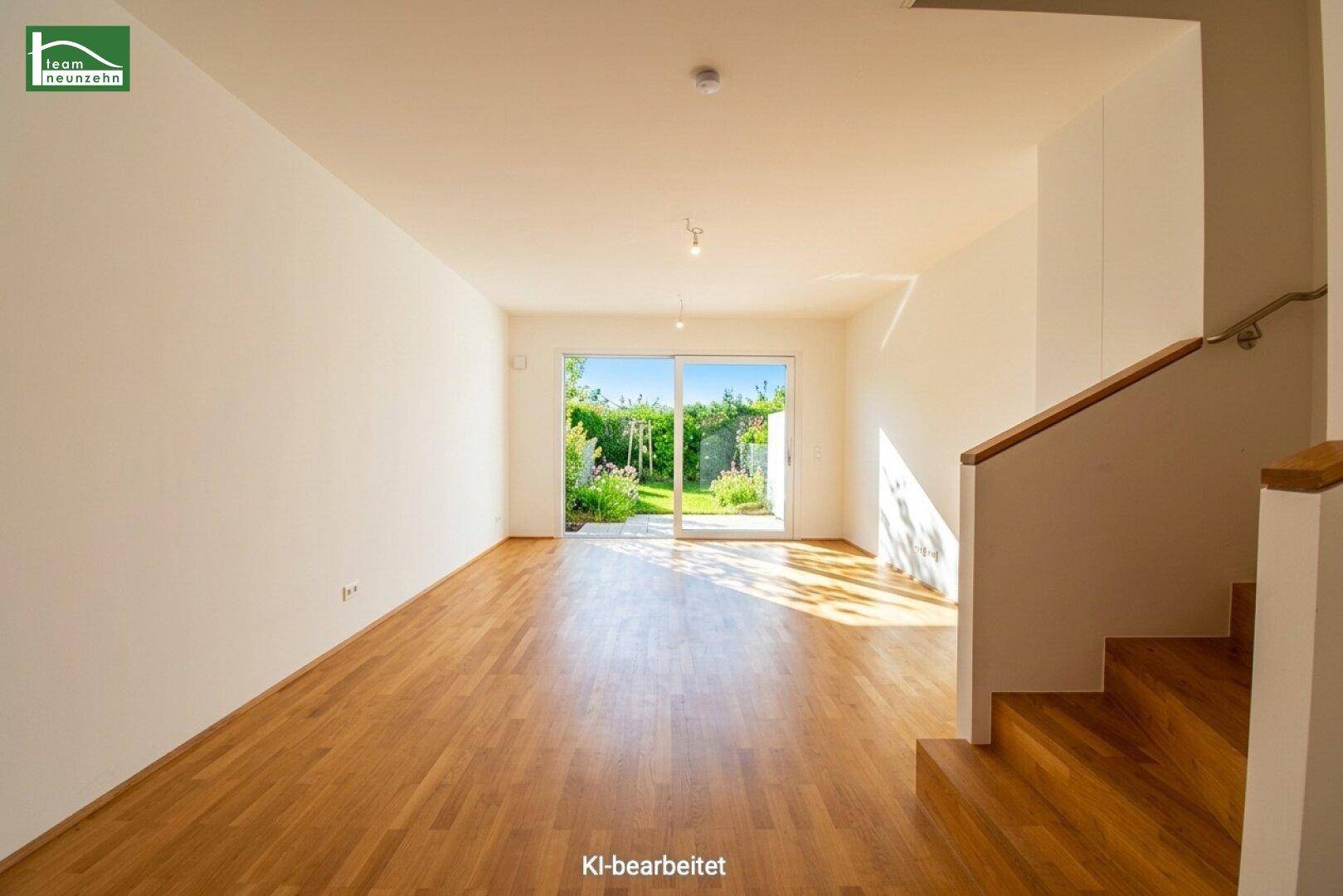 Heller Wohnraum mit Holzboden, Treppe und großen Fenstern zum grünen Außenbereich.