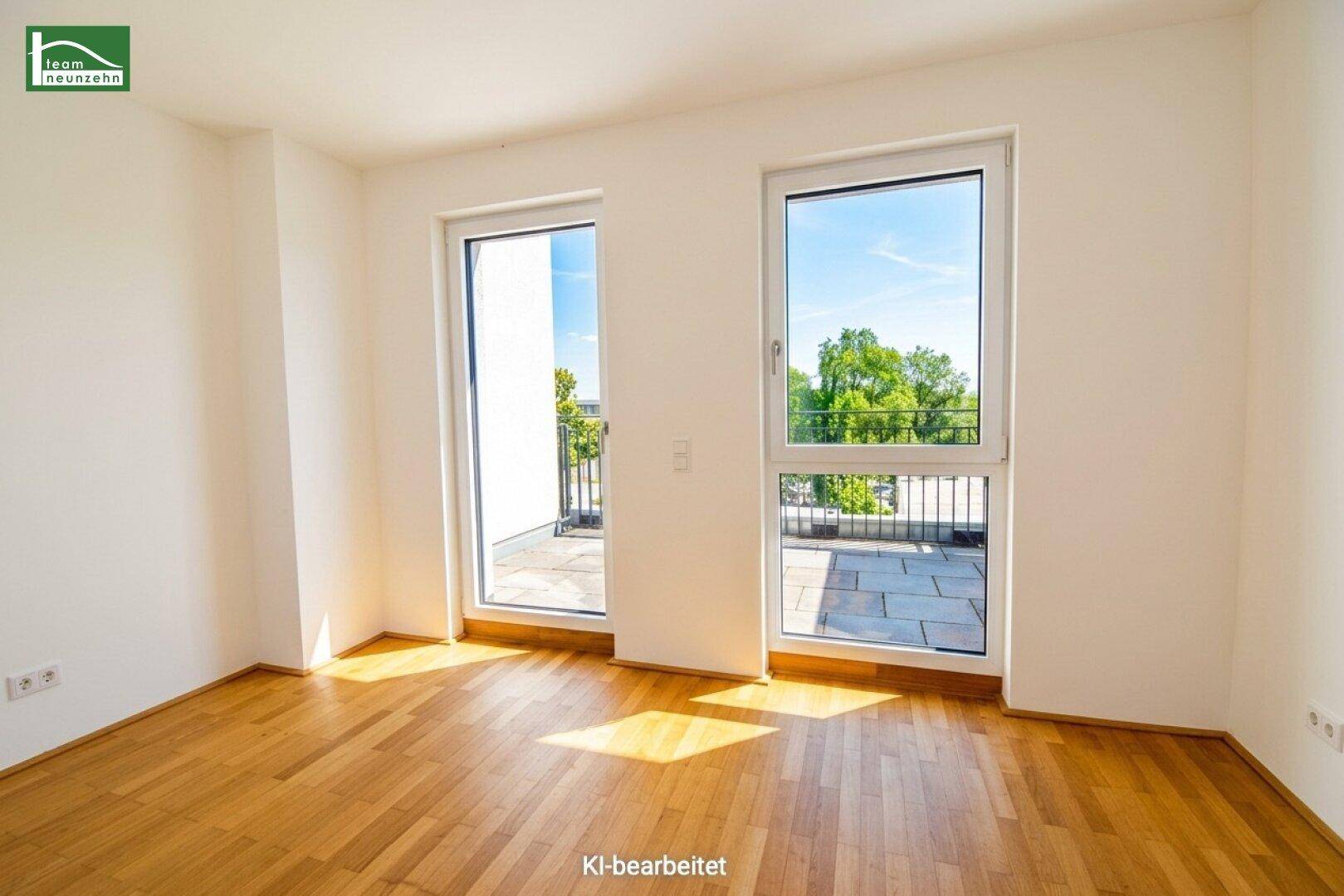 Heller, leerer Raum mit Holzfußboden und großen Fenstern, die Zugang zur Terrasse bieten.