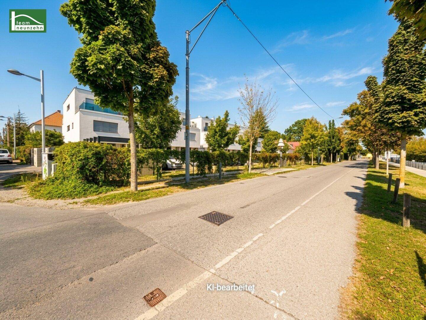 Ruhige Wohnstraße mit Bäumen und modernen Gebäuden im Hintergrund unter blauem Himmel.