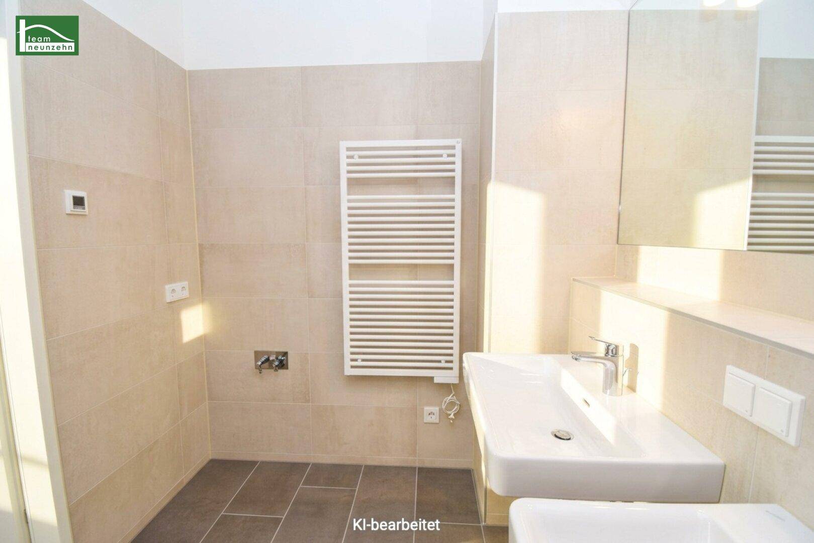 Helles Badezimmer mit Einzelwaschbecken, großem Spiegel und beheiztem Handtuchhalter, in Beigetönen gehalten.