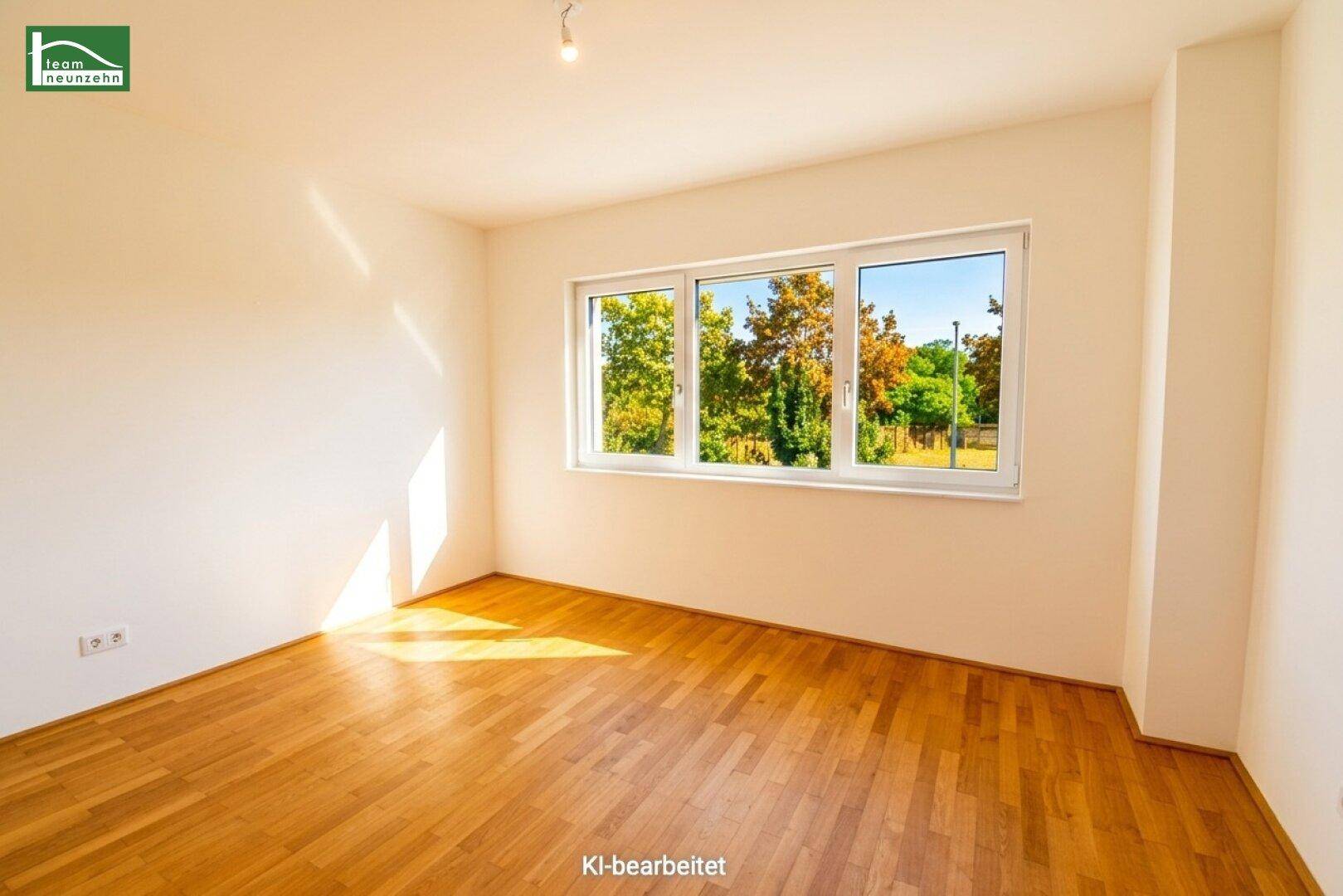 Geräumiges Zimmer mit Holzboden und großem Fenster, bietet viel Tageslicht und Blick ins Grüne.
