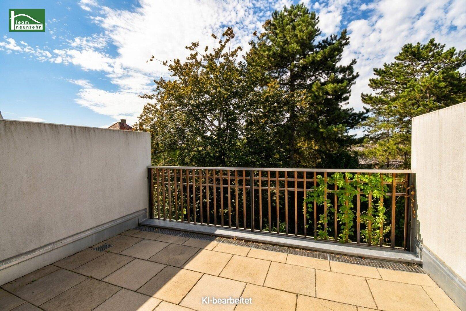 Geräumige Terrasse mit Fliesenboden und Metallgeländer, umgeben von grünen Bäumen unter blauem Himmel.