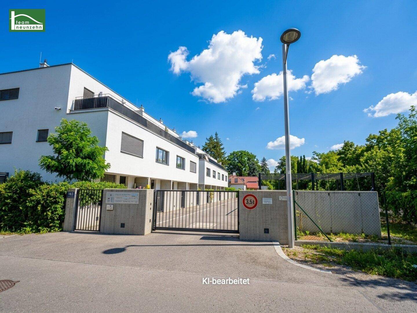 Eingangstor zu einer modernen Wohnanlage mit weißen Gebäuden und gepflegter Außenanlage.