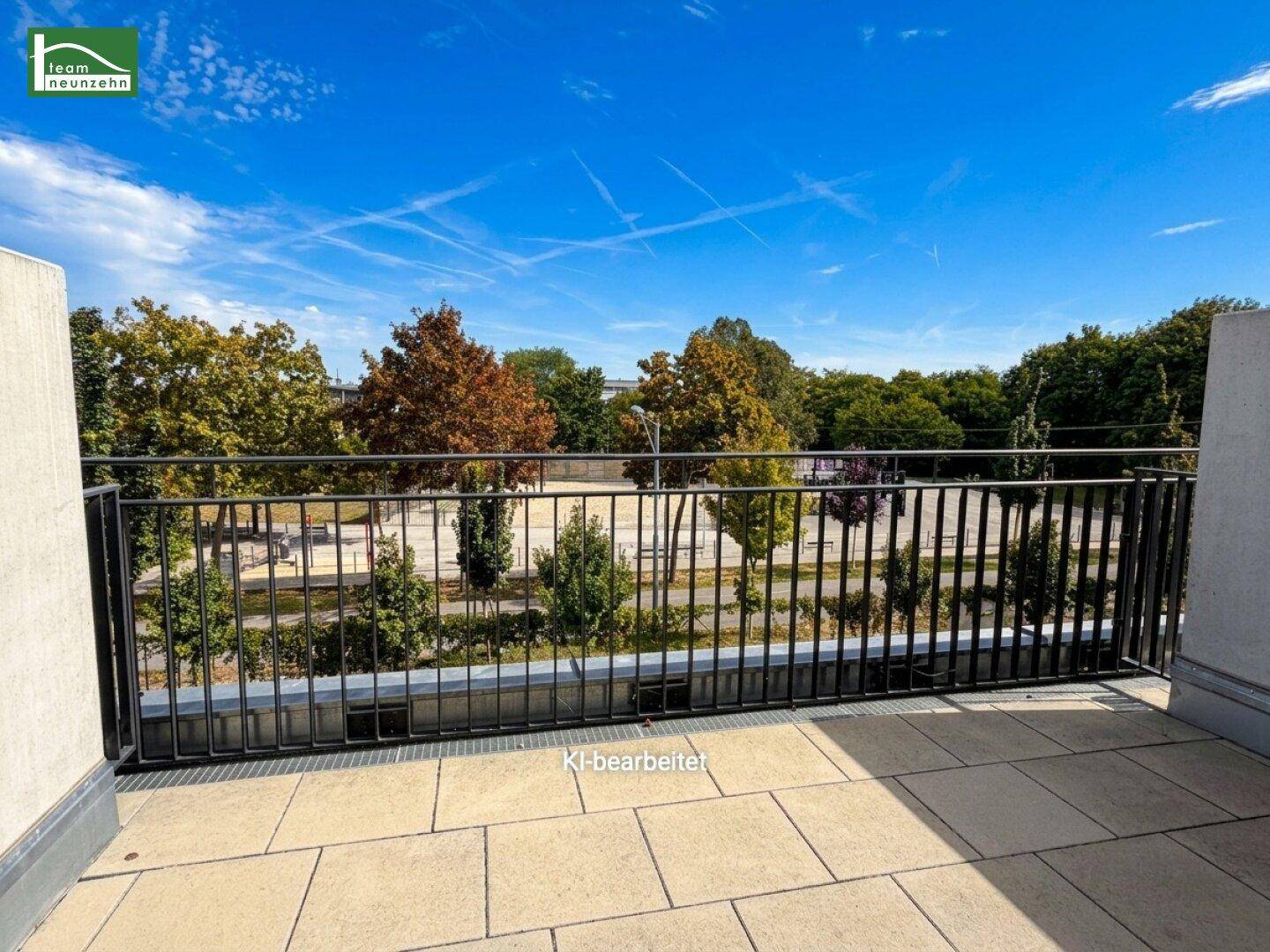 Geräumige geflieste Terrasse mit schwarzem Geländer und Blick auf eine grüne Parklandschaft.