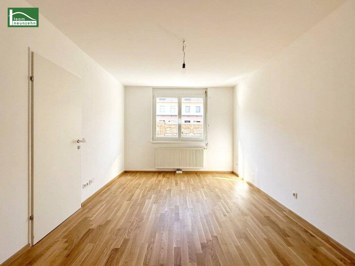 Leerer Raum mit Holzboden, einem Fenster und Heizkörper, ideal als Schlaf- oder Arbeitszimmer.