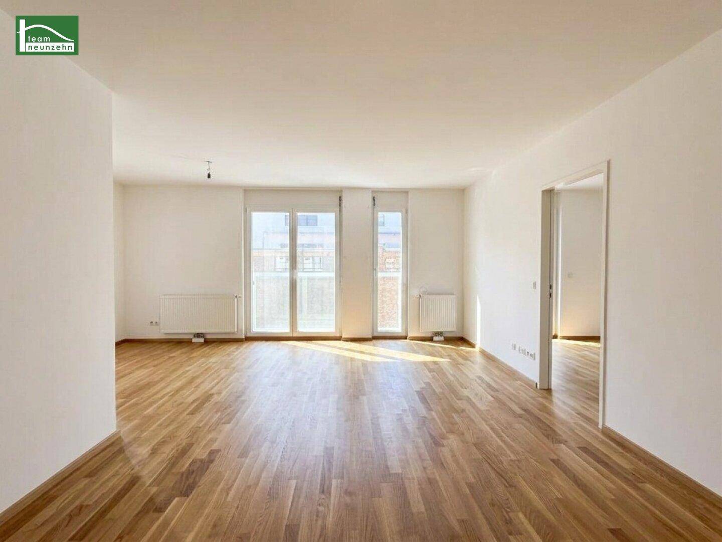 Heller, leerer Raum mit Holzboden und großen Fenstertüren, die viel Tageslicht hereinlassen.
