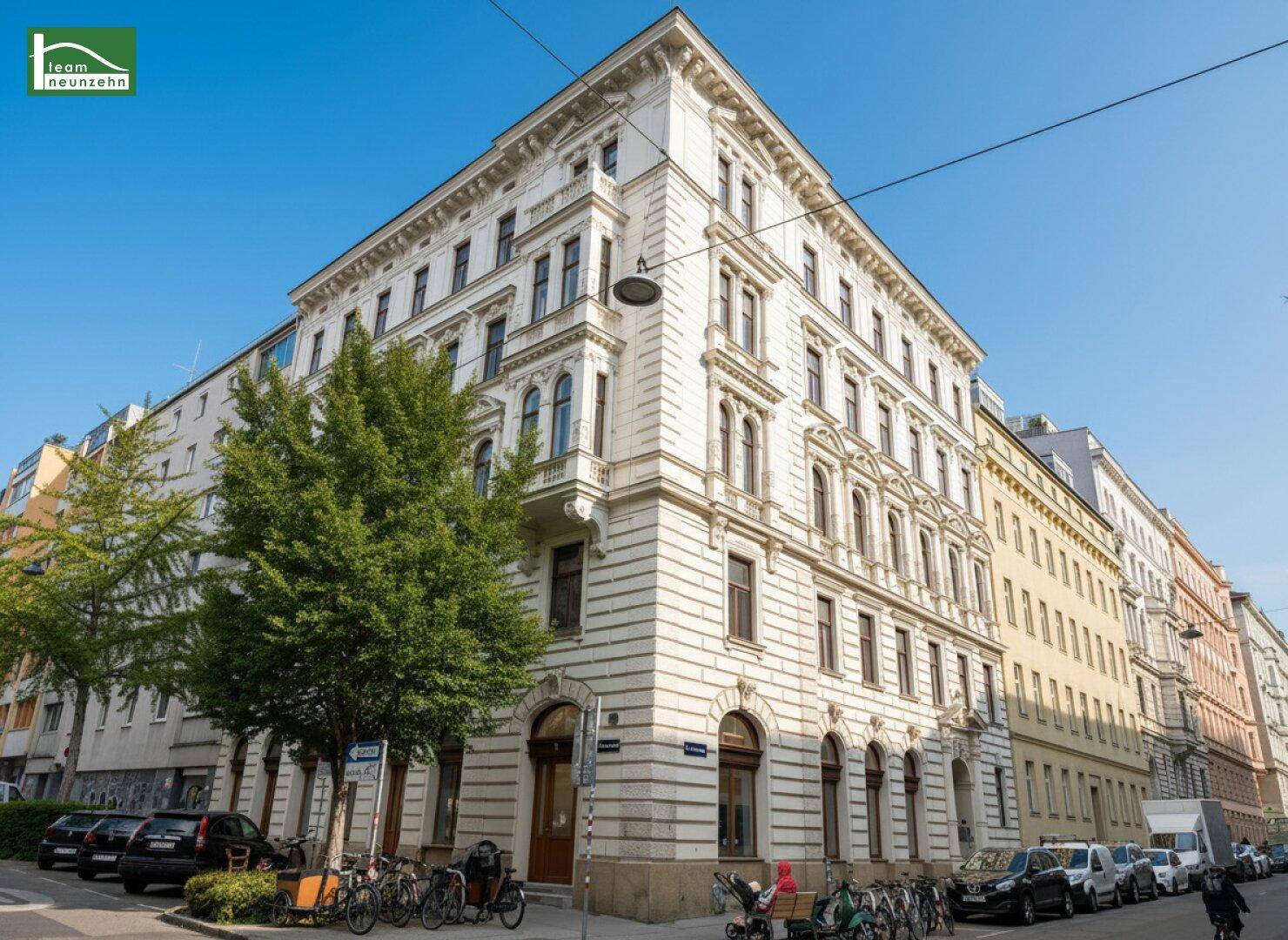 Historisches Eckgebäude an einer belebten Straße mit geparkten Fahrrädern und Autos.