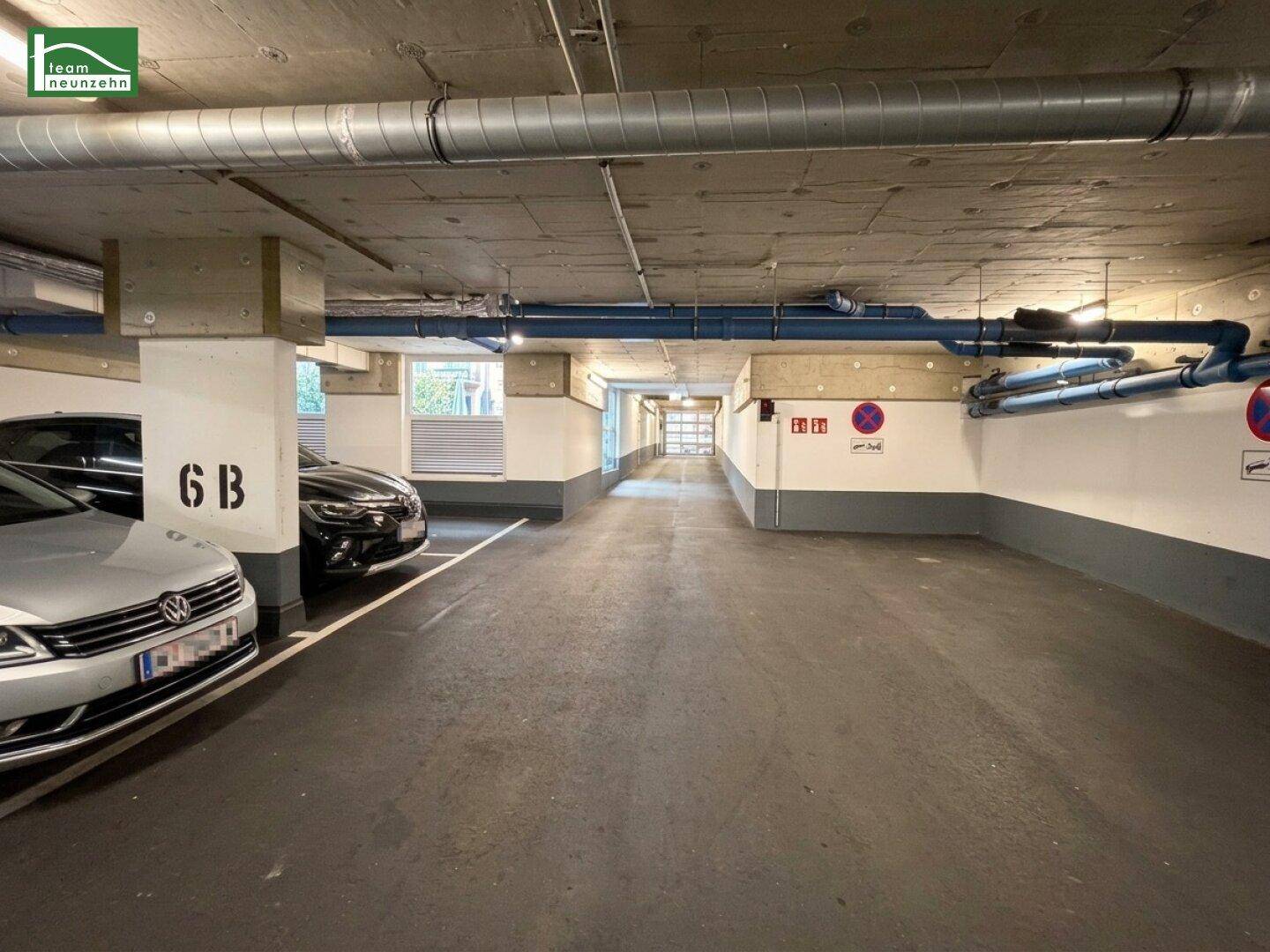 Langer Gang in einer Tiefgarage mit Stellplätzen und sichtbaren Lüftungsrohren.