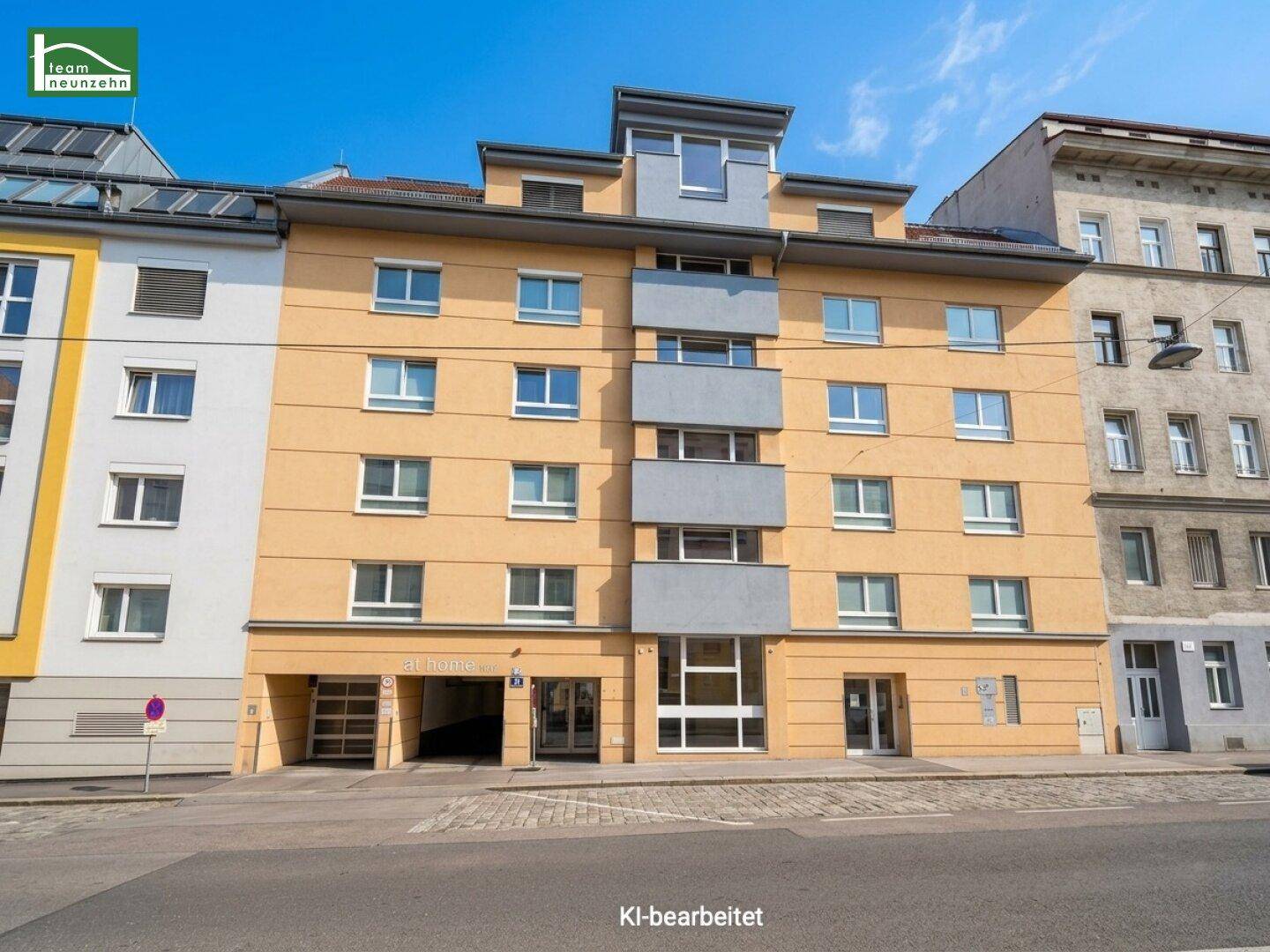 Modernes Wohngebäude mit gelber Fassade, grauen Balkonen und Tiefgarageneinfahrt.