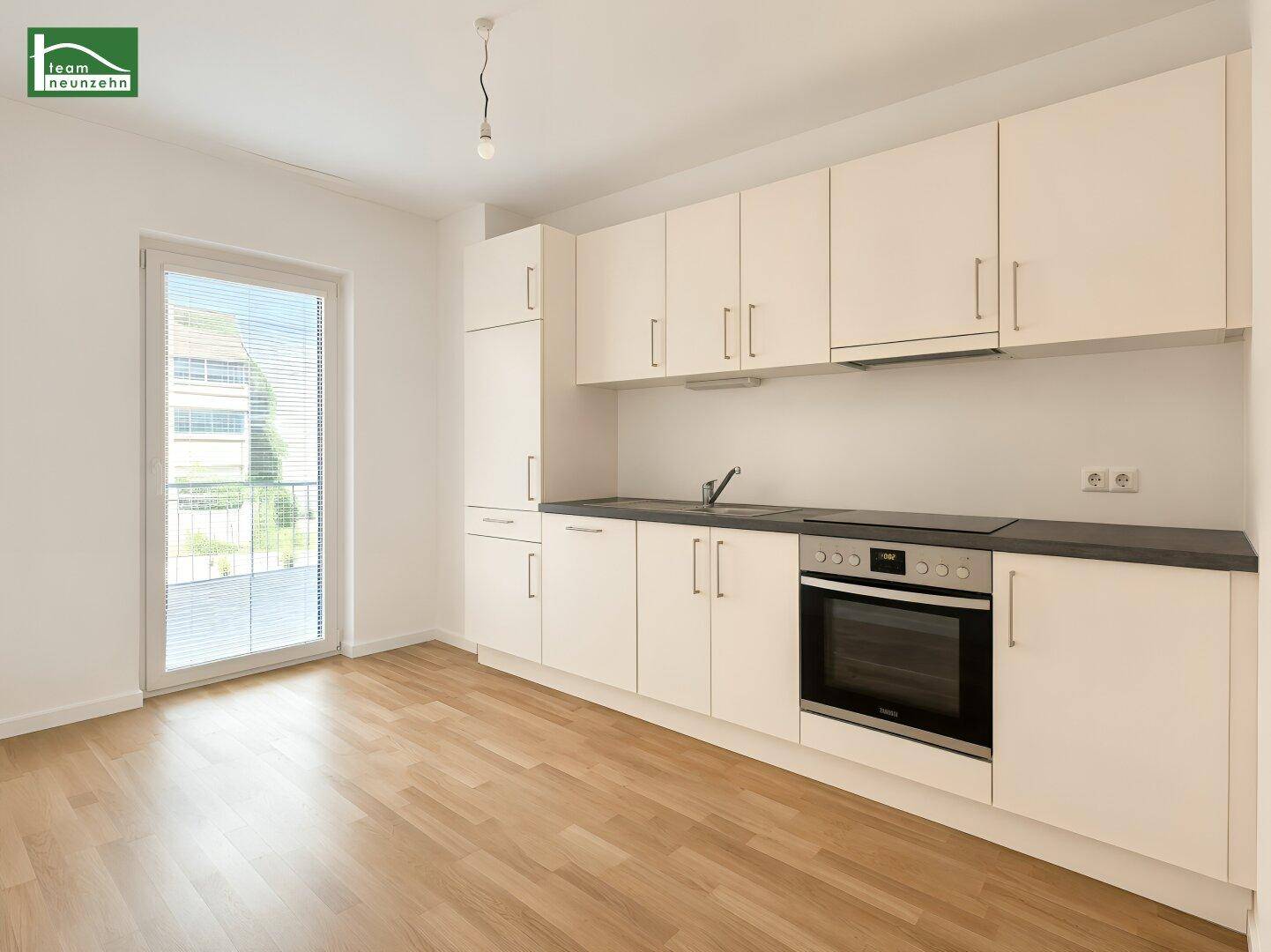 Helle Küchenzeile mit weißen Schränken, Kochfeld und Zugang zum Balkon.