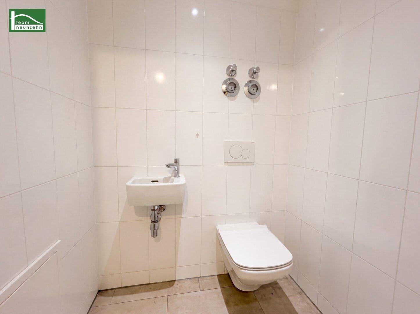 Modernes Gäste-WC mit weißen Fliesen, wandhängendem WC und kleinem Waschbecken.