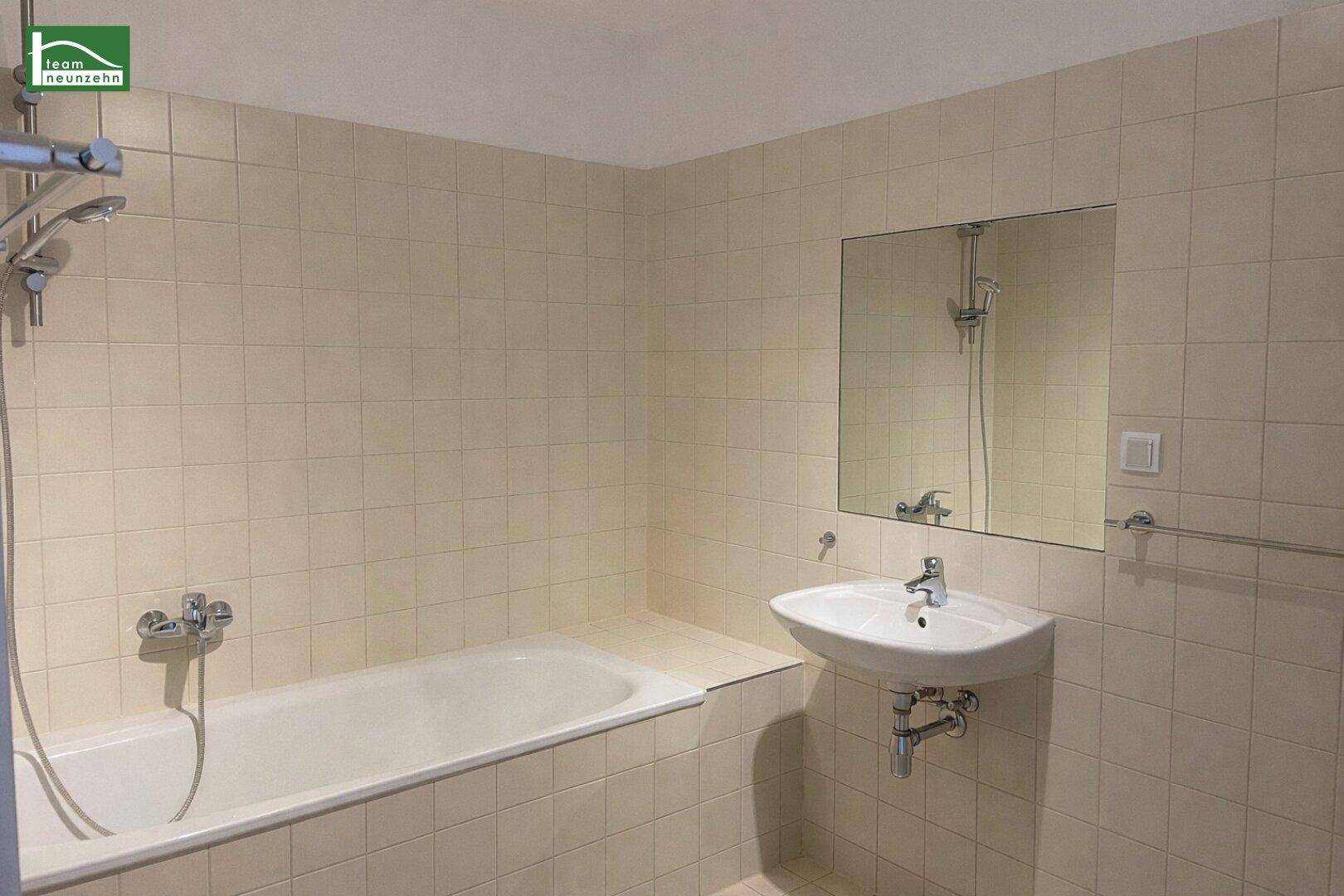 Badezimmer mit beigefarbenen Fliesen, Badewanne mit Duschfunktion und einem Waschbecken.