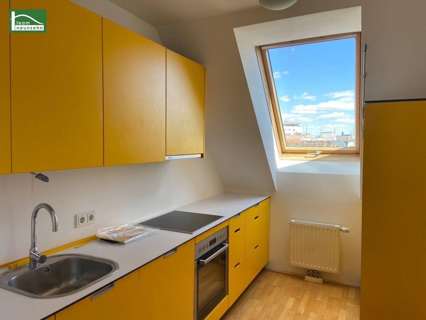 Helle Küche mit gelben Schränken, Einbaugeräten und einem Dachfenster für viel Tageslicht.