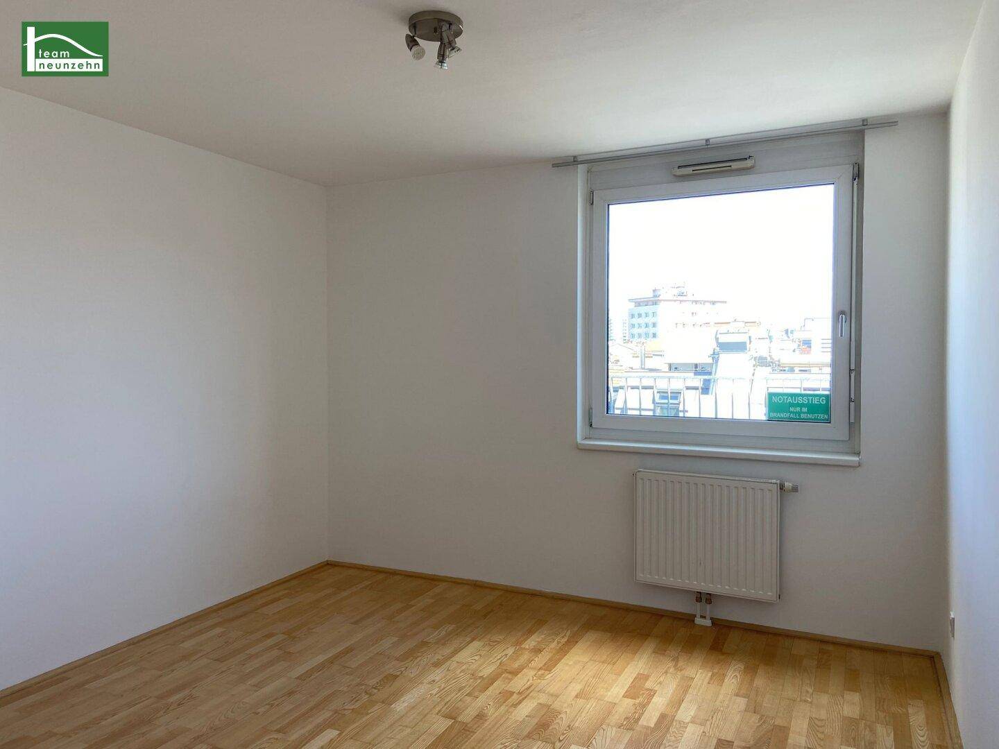 Helles Zimmer mit Parkettboden, weißen Wänden und einem Fenster mit Blick auf die Umgebung.