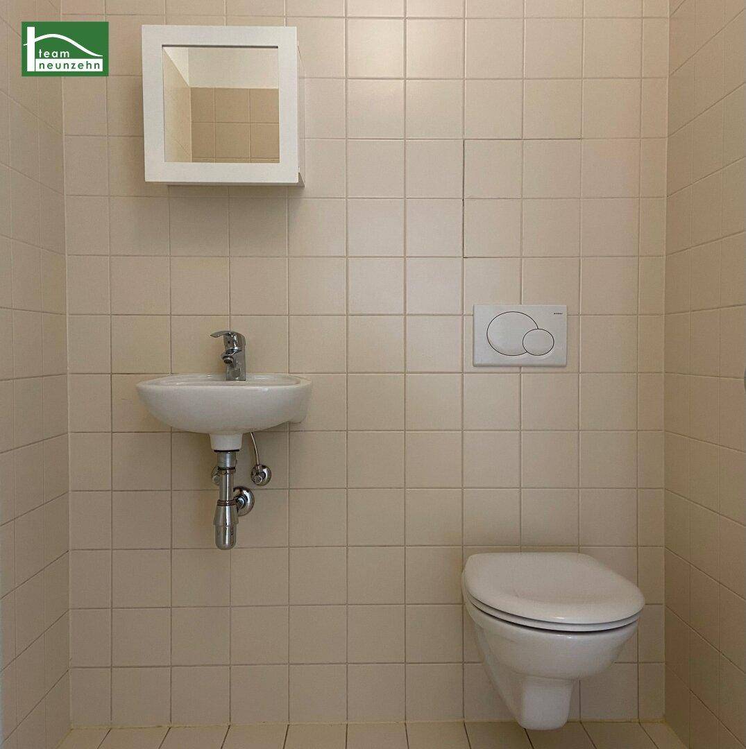 Separates WC mit beigefarbenen Fliesen, wandhängendem WC und kleinem Waschbecken.