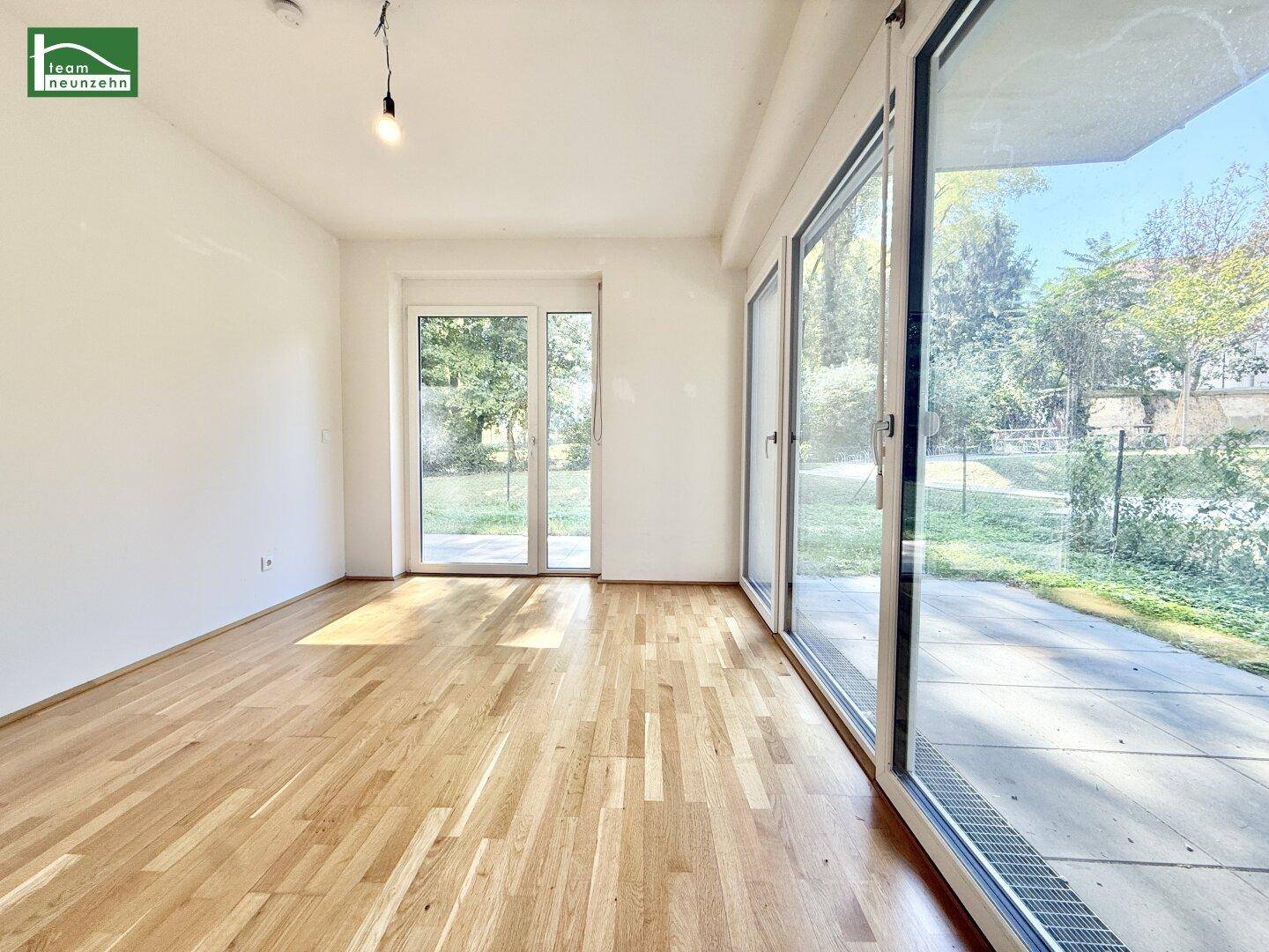 Lichtdurchfluteter Raum mit Parkettboden und großen Fensterfronten zum Außenbereich.