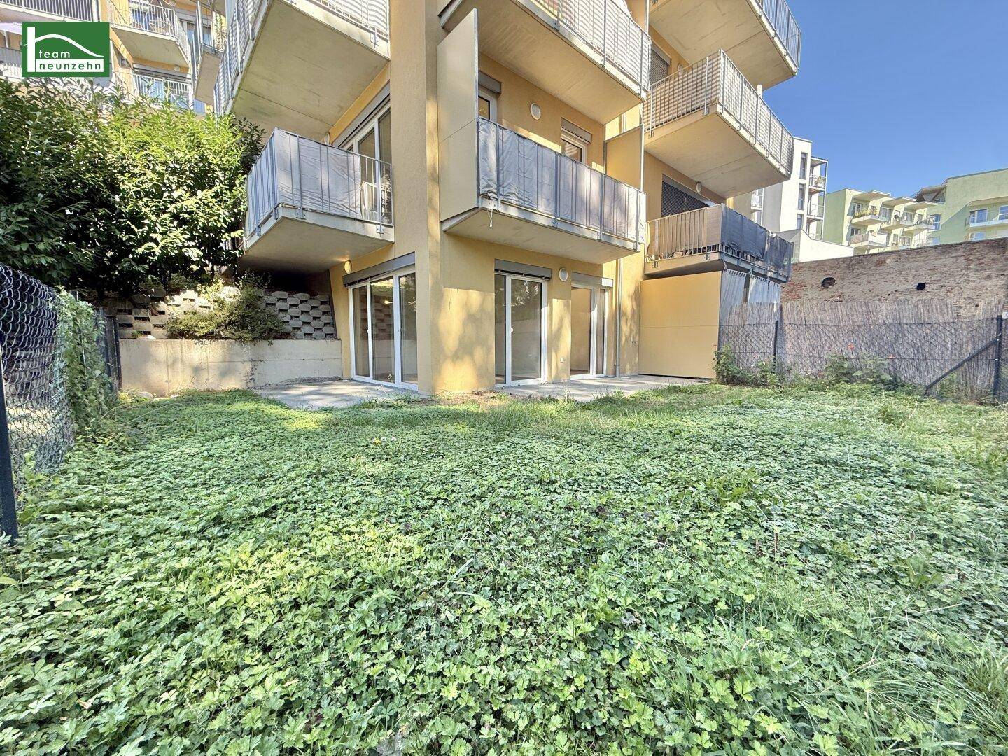 Grüner Gartenbereich im Erdgeschoss mit direktem Zugang zu den Wohnungen und Blick auf die Balkone.