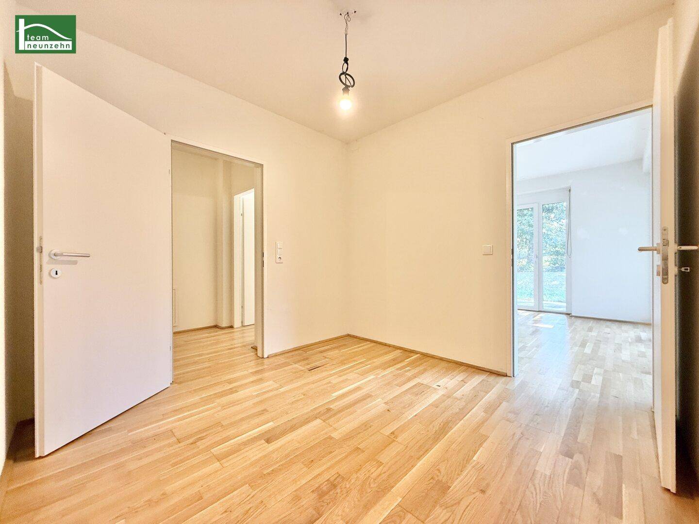 Geräumiges Zimmer mit Holzboden und mehreren Türöffnungen, die zu weiteren hellen Räumen führen.
