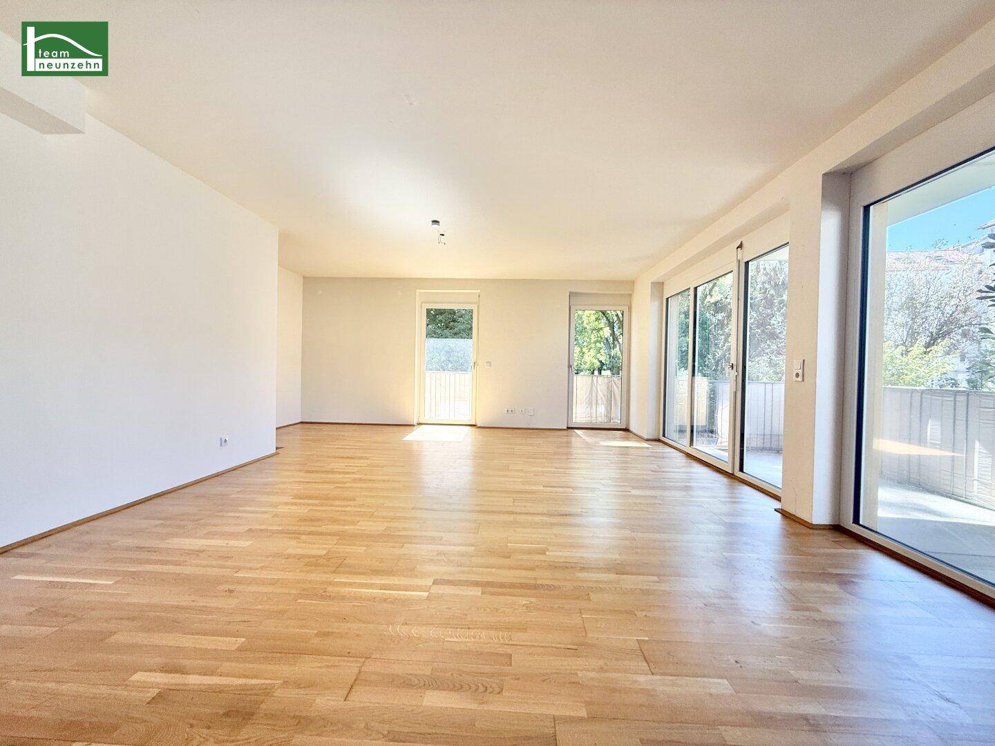Großzügiger, heller Raum mit Holzboden und mehreren Zugängen zu Außenbereichen, ideal für flexible Gestaltung.