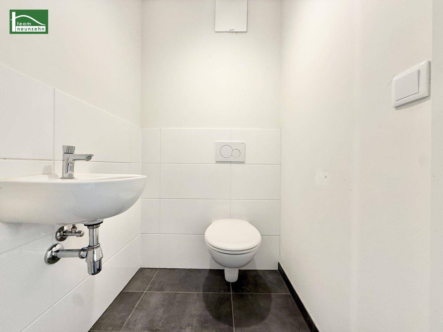 Modernes Gäste-WC mit wandhängender Toilette, kleinem Waschbecken und weißen Wandfliesen.