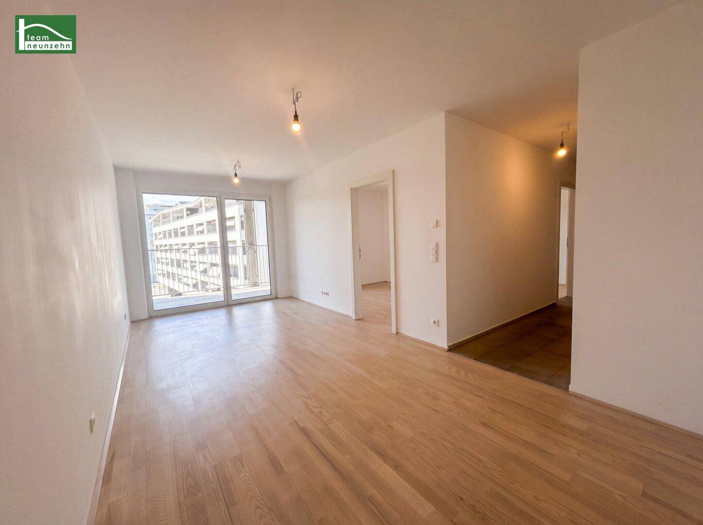 Helles Wohnzimmer mit Parkettboden, weißen Wänden und Zugang zu einem Balkon.