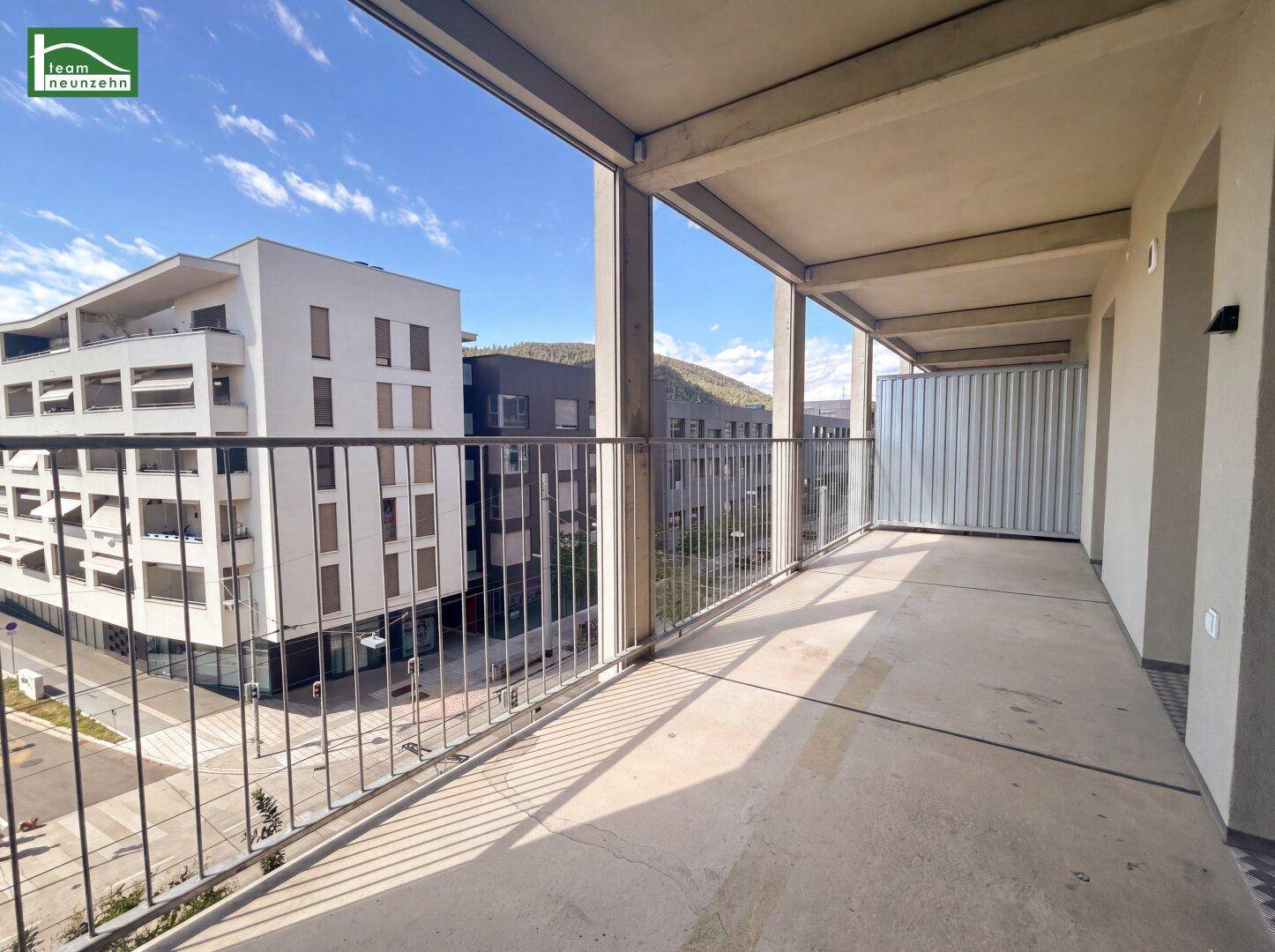 Geräumiger Balkon mit Betonboden und Blick auf moderne Gebäude und die Stadt.