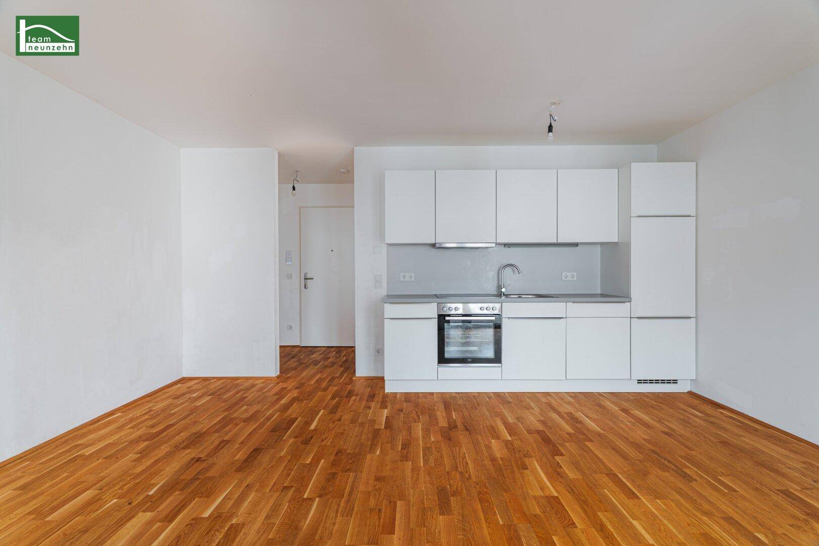 Moderne Einbauküche mit weißen Schränken, integriertem Backofen und hellem Parkettboden.