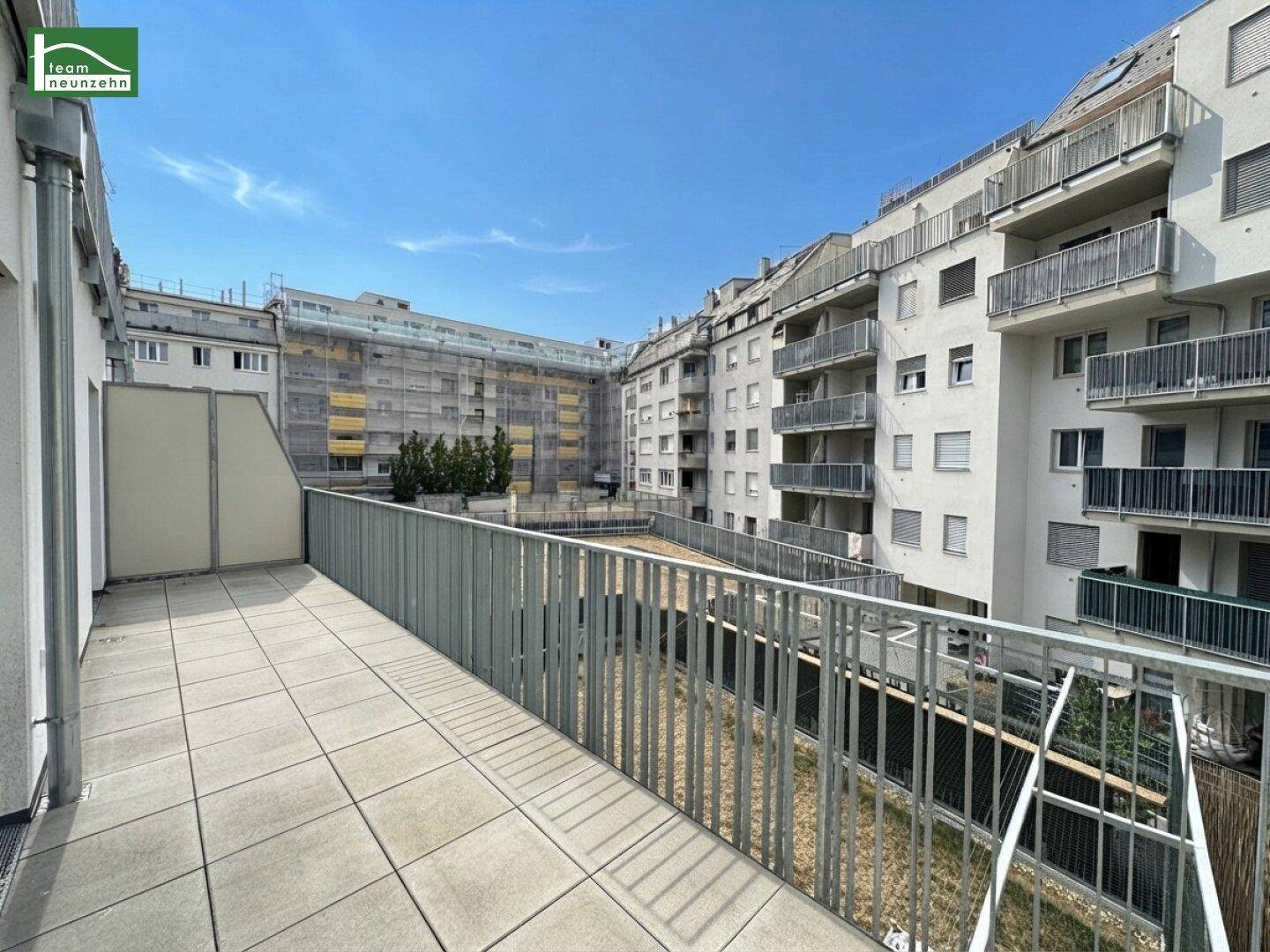 Geräumige geflieste Terrasse mit Metallgeländer und Blick auf den Innenhof des Gebäudekomplexes.