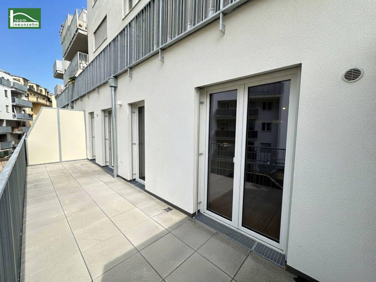 Heller Terrassenbereich mit Fliesenboden und großen Glastüren, die in die Wohnräume führen.