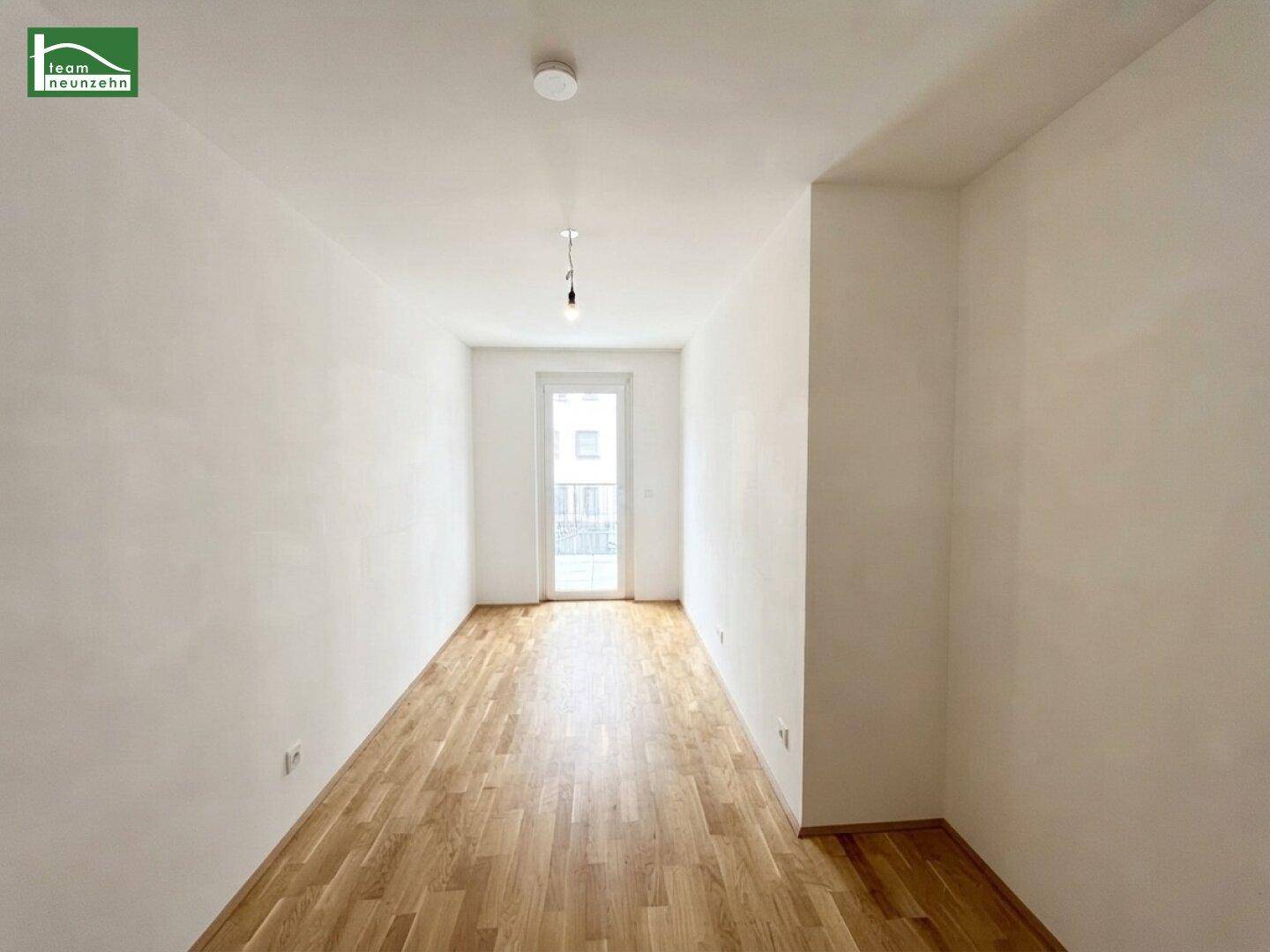 Helles, leeres Zimmer mit Parkettboden und einer Fenstertür, die ins Freie führt.