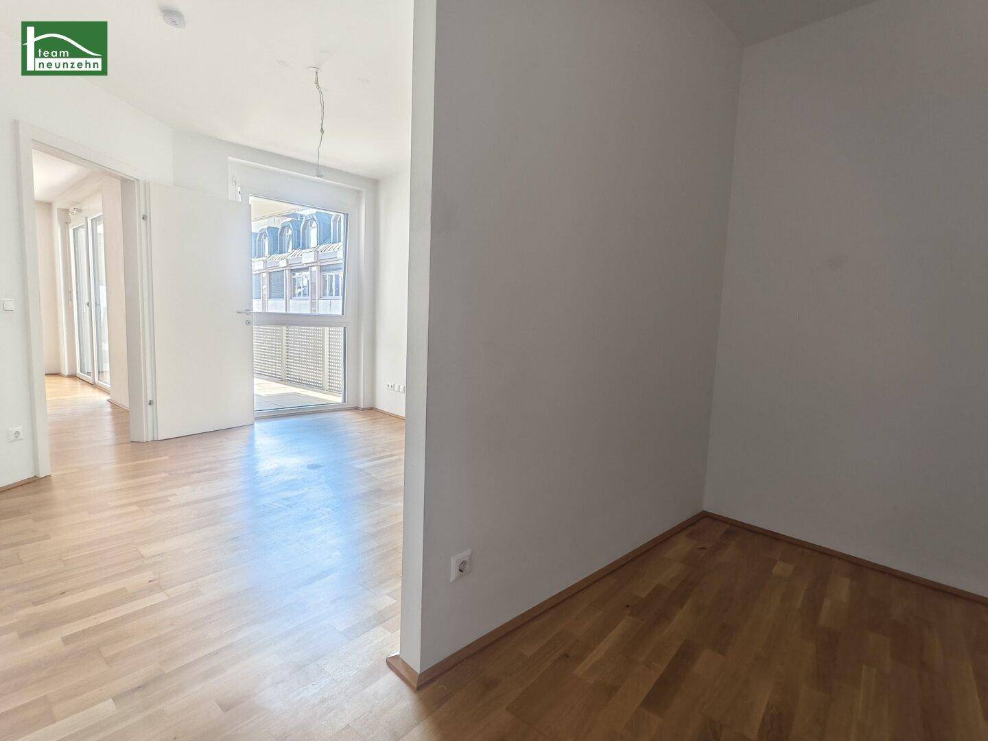Offener Wohnbereich mit Parkettboden und Zugang zu einem Balkon, der viel Tageslicht bietet.