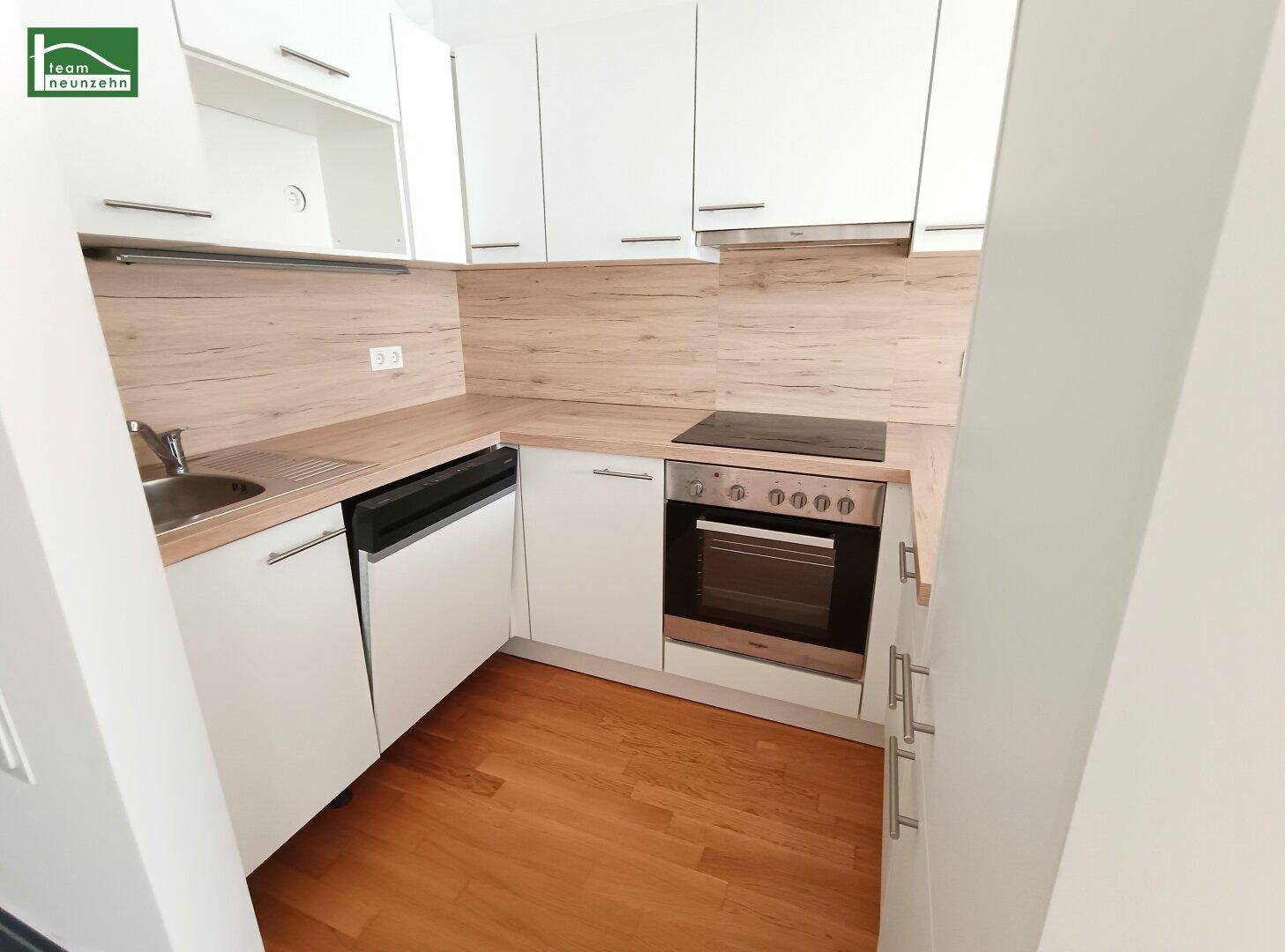 Kompakte, moderne Küchenzeile mit weißen Schränken, Holzarbeitsplatte und integrierten Geräten.