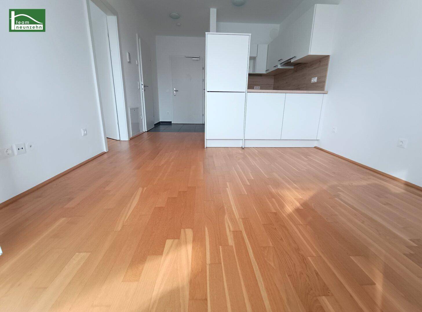 Heller Wohnbereich mit Parkettboden und integrierter Küchenzeile in modernem Design.