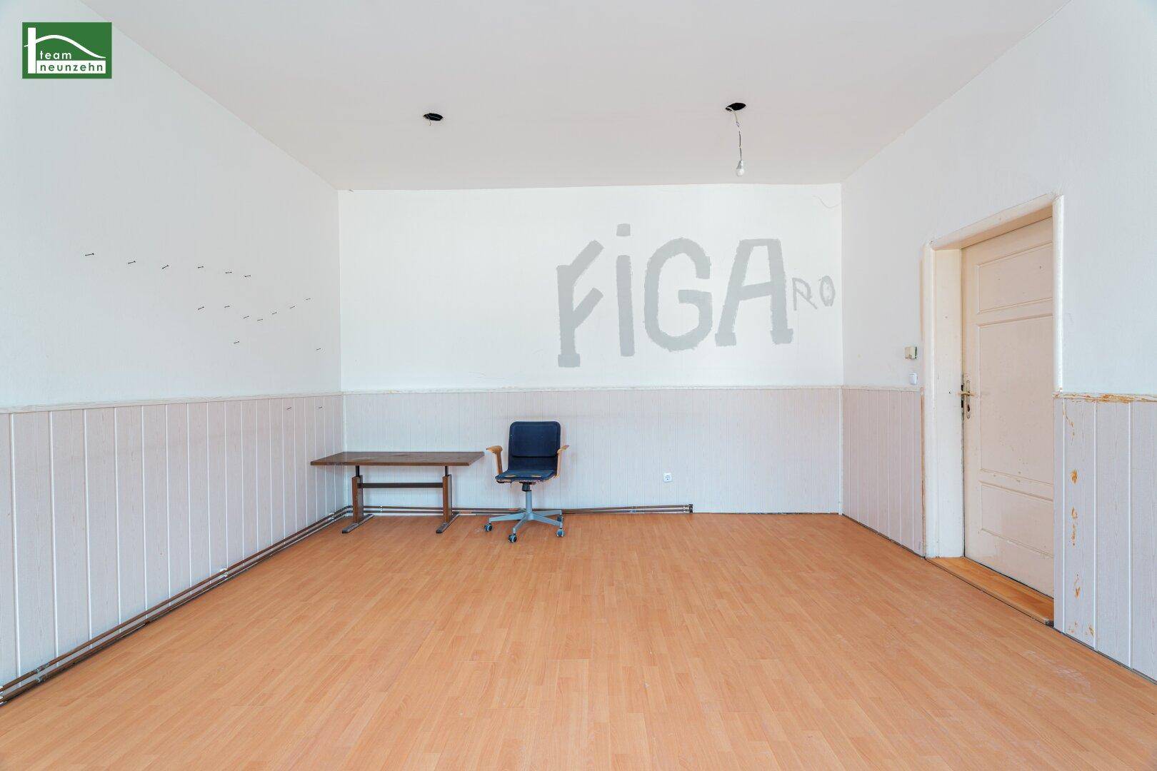 Geräumiger, leerer Raum mit einer Wandbeschriftung, Holzvertäfelung und Laminatboden.