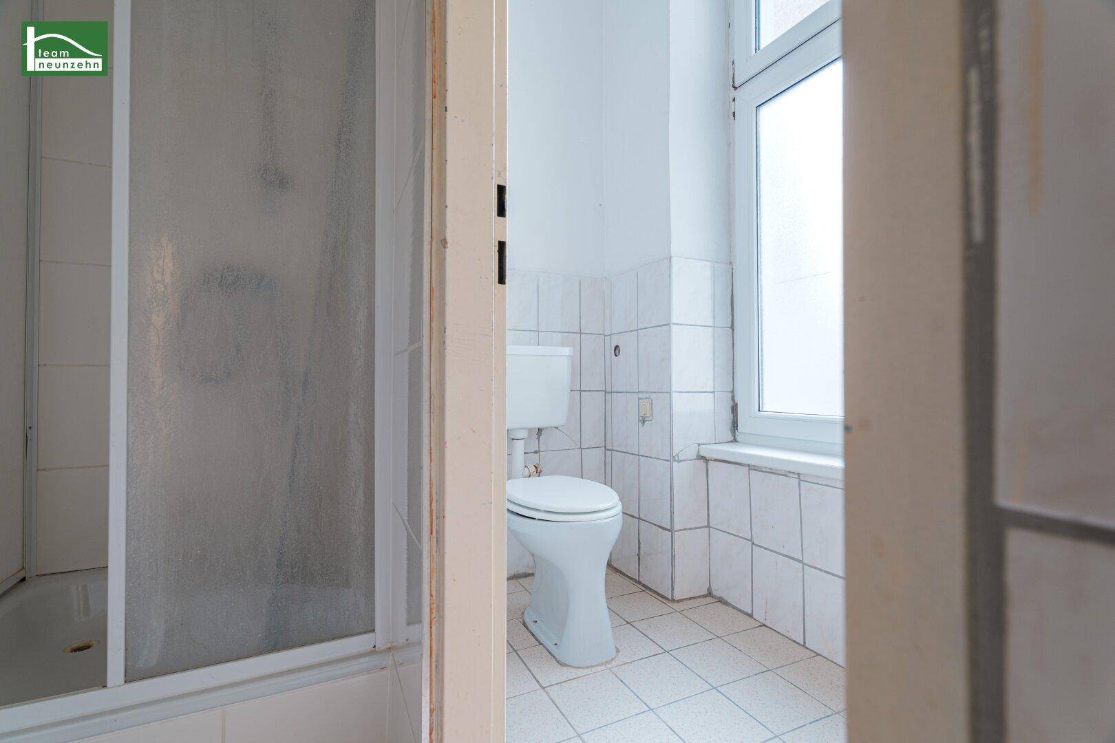 Badezimmer mit weißen Fliesen, Toilette und Duschkabine, durch einen Türrahmen sichtbar.