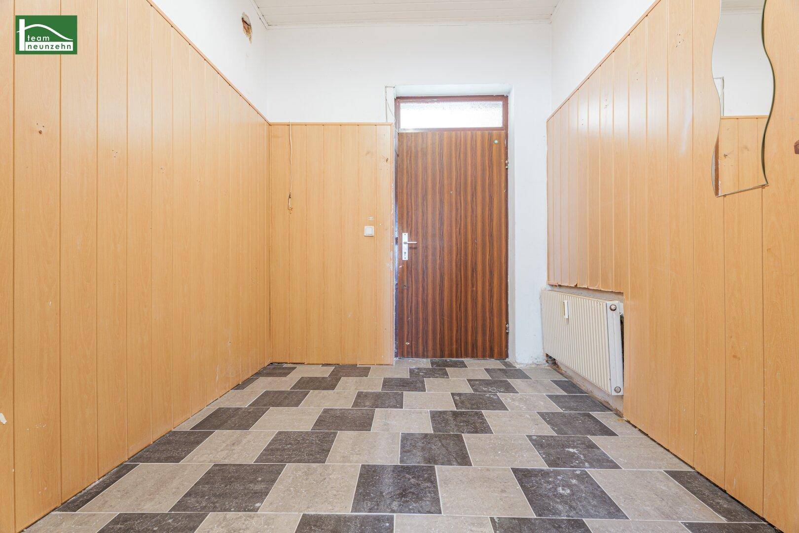 Flur mit Holzvertäfelung, gemusterten Fliesen und einer Holztür mit Oberlicht.
