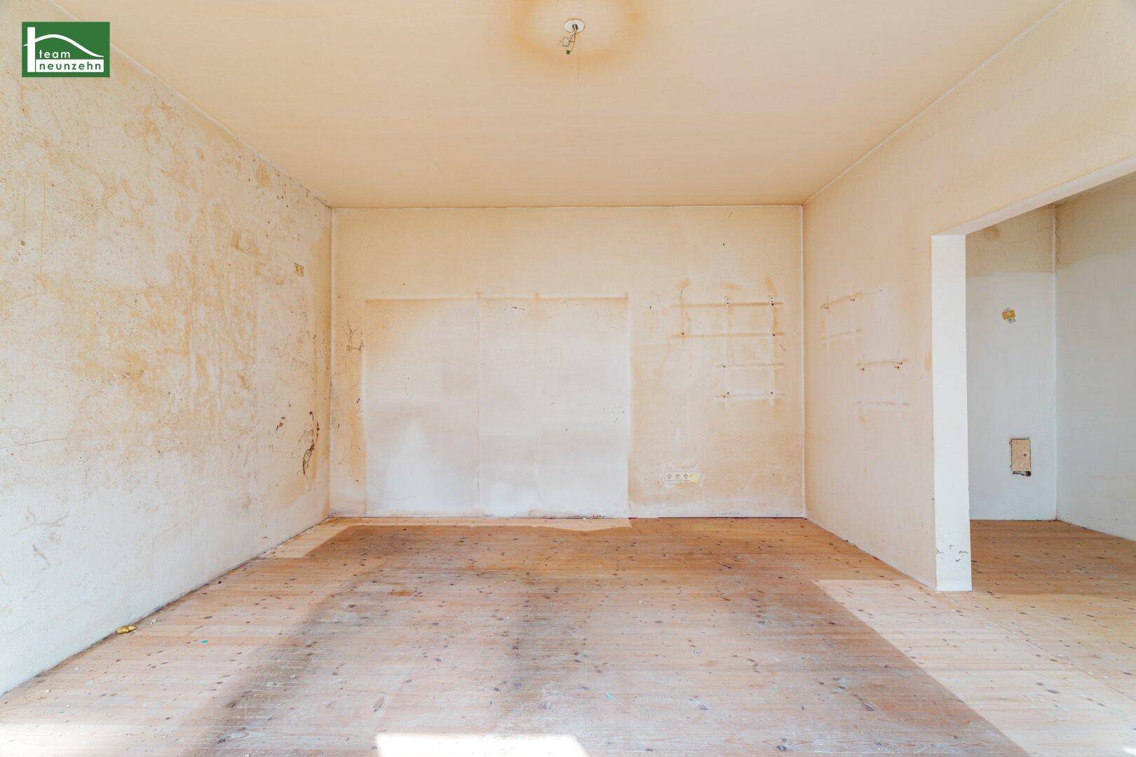 Unmöblierter Raum mit abgenutztem Holzboden und Spuren früherer Einbauten, renovierungsbedürftig.