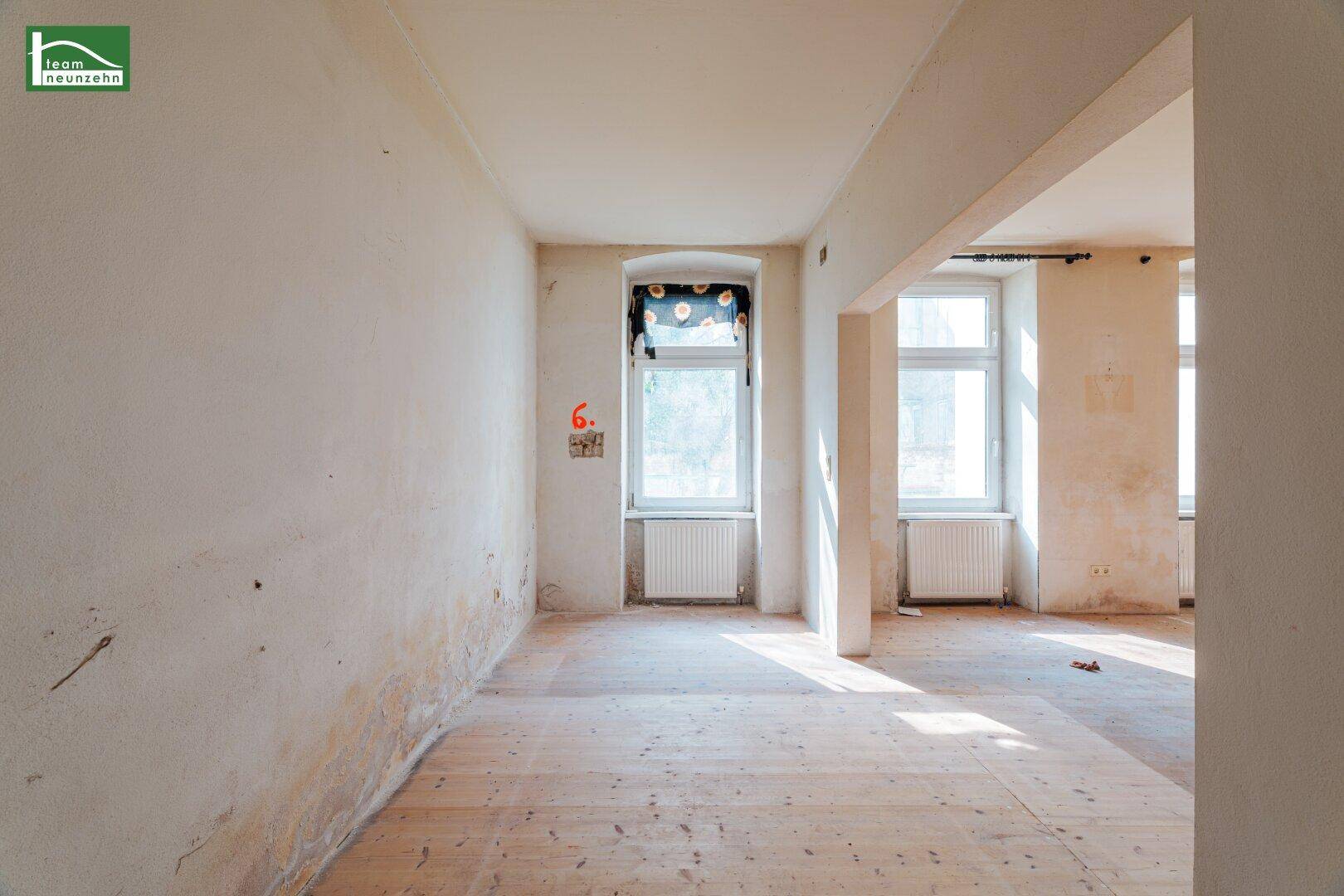 Lichtdurchfluteter Raum mit Holzdielenboden und Blick auf die Umgebung, renovierungsbedürftig.