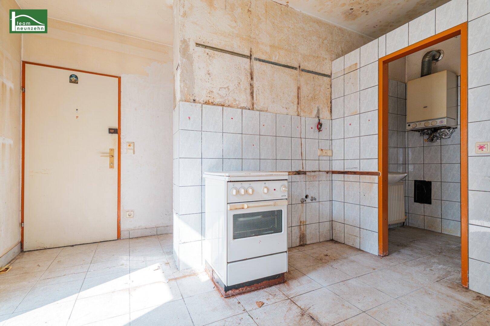 Renovierungsbedürftige Küche mit Fliesenboden, altem Herd und Gastherme an der Wand.