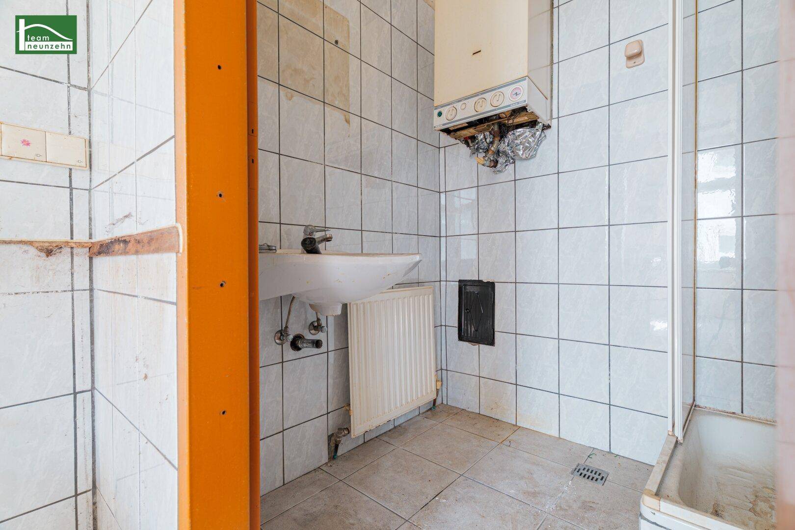 Einfaches Badezimmer mit weißen Fliesen, Waschbecken, Heizkörper und alter Badewanne.